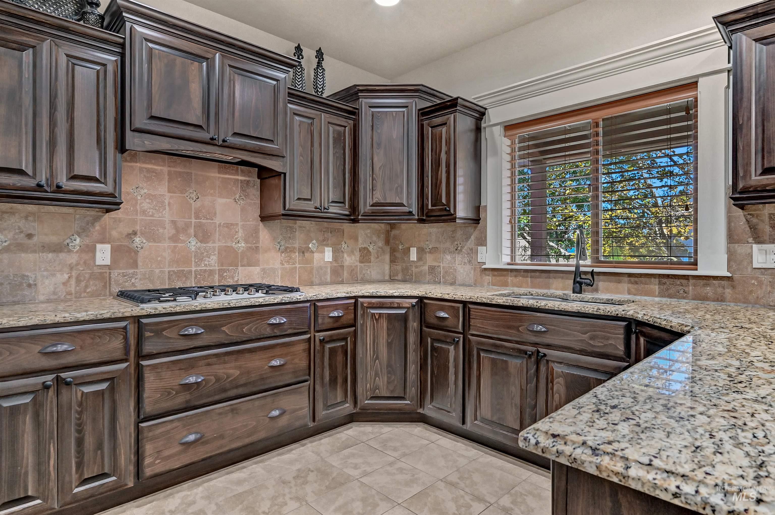 Kitchen with dark brown cabinets, backsplash, light tile patterned floors, light stone counters, and recessed lighting
