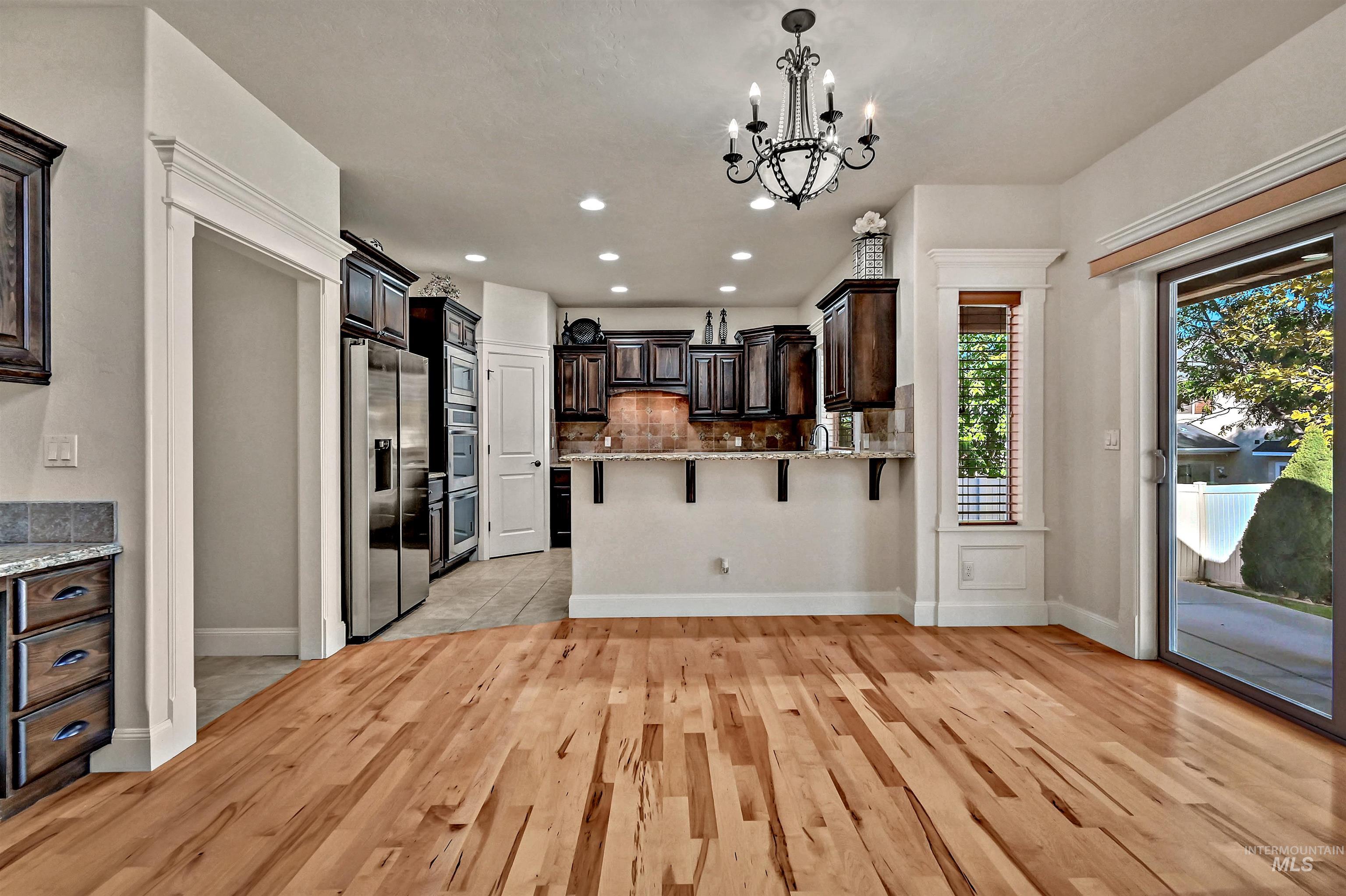 Kitchen with decorative backsplash, appliances with stainless steel finishes, a chandelier, hanging light fixtures, and a breakfast bar