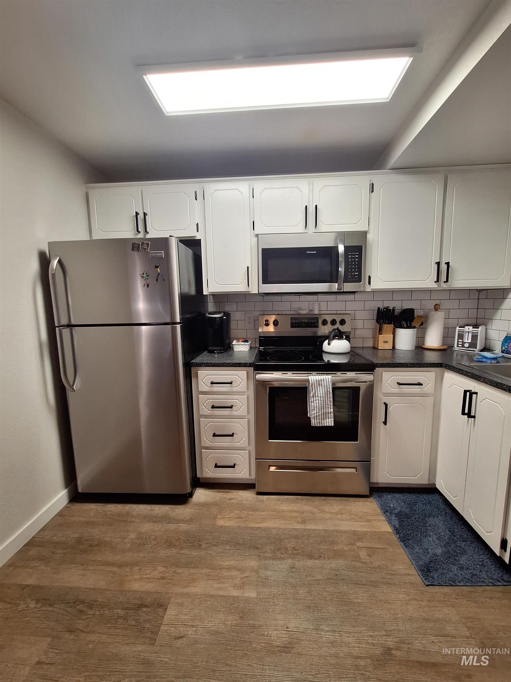 Kitchen featuring appliances with stainless steel finishes, light wood-type flooring, white cabinets, and tasteful backsplash
