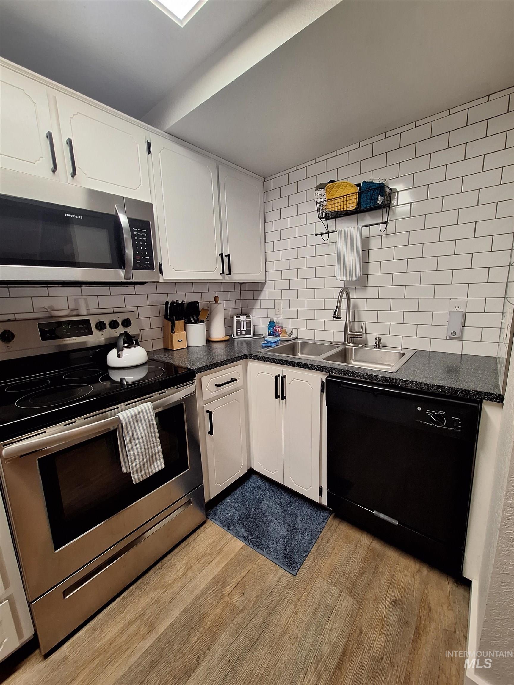 Kitchen featuring stainless steel appliances, dark countertops, light wood-type flooring, white cabinets, and tasteful backsplash