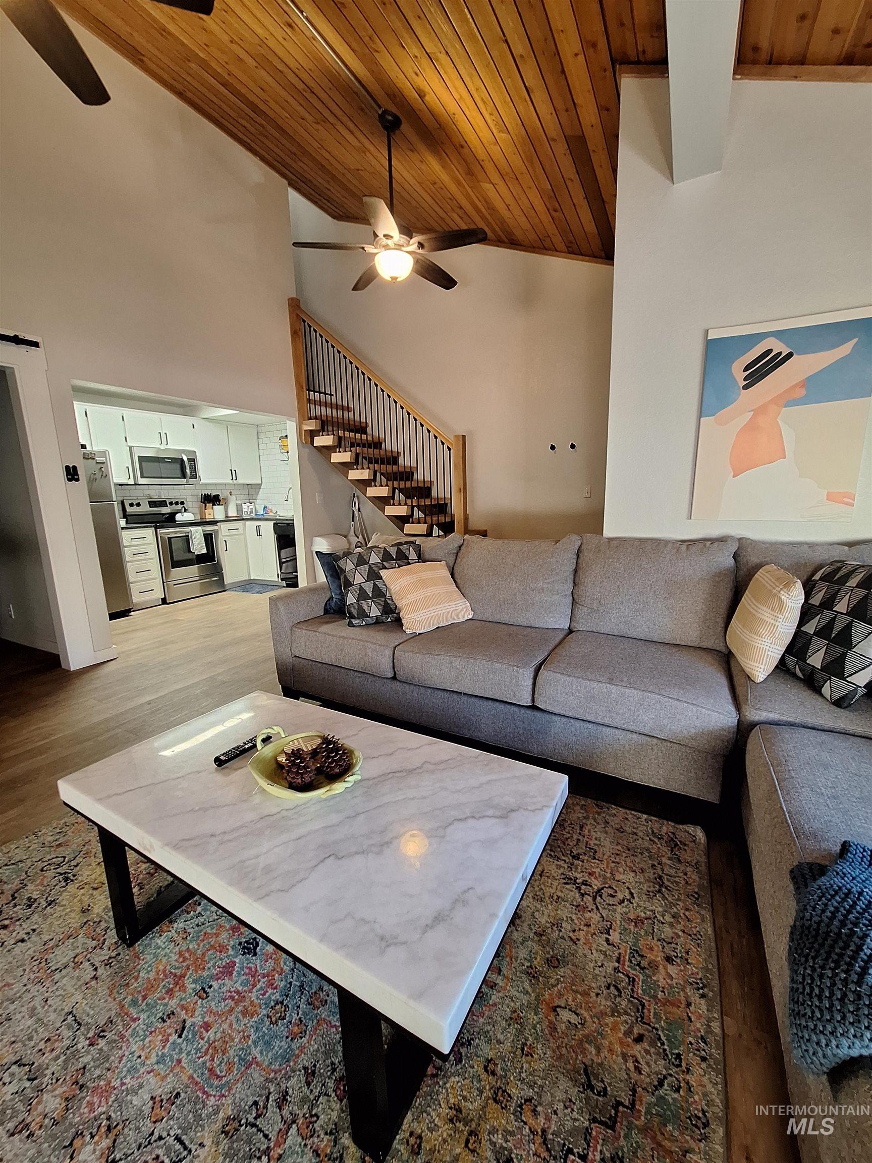 Living room featuring wooden ceiling, high vaulted ceiling, stairway, wood finished floors, and ceiling fan