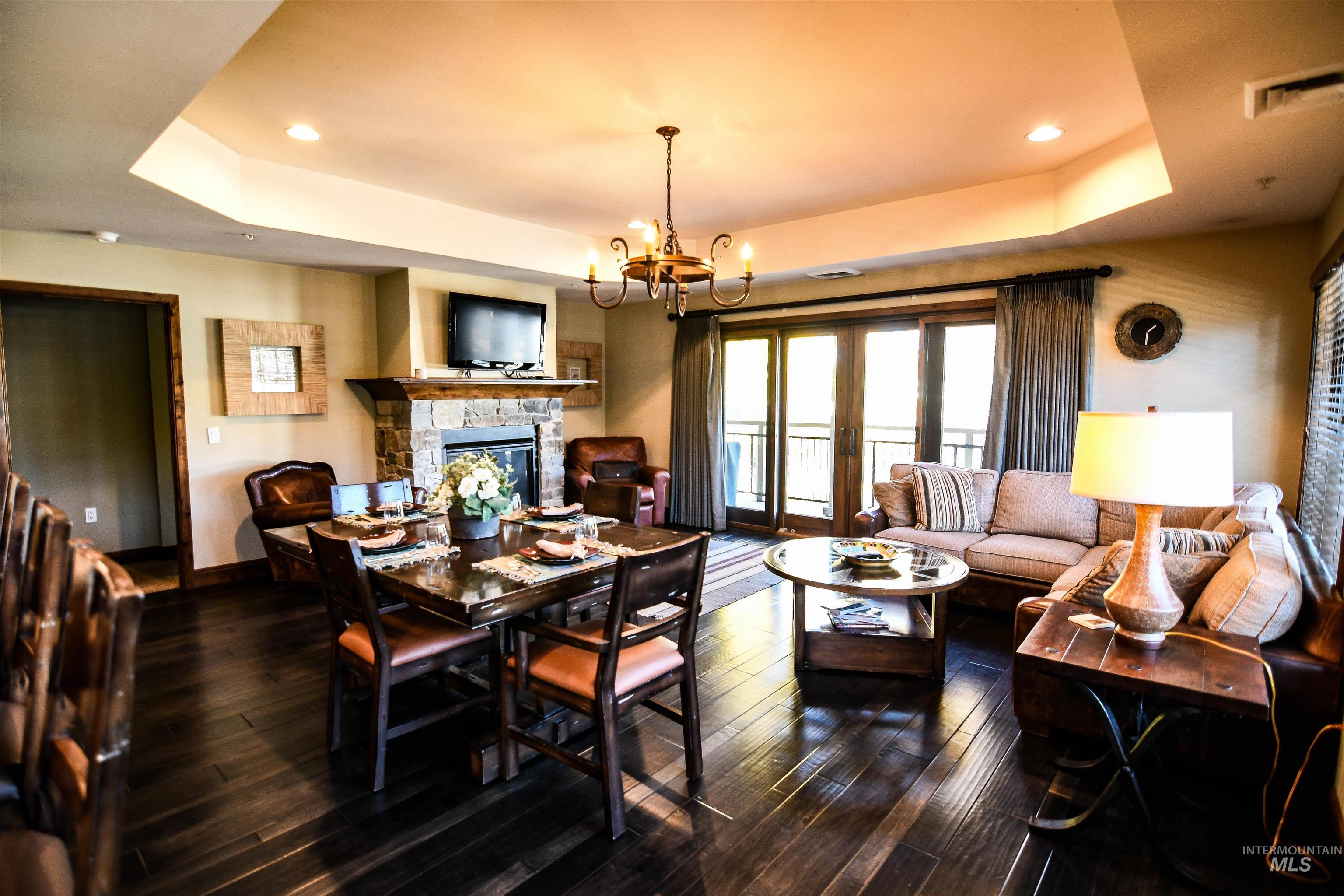 Dining space with a raised ceiling, a stone fireplace, a chandelier, dark wood-style floors, and recessed lighting