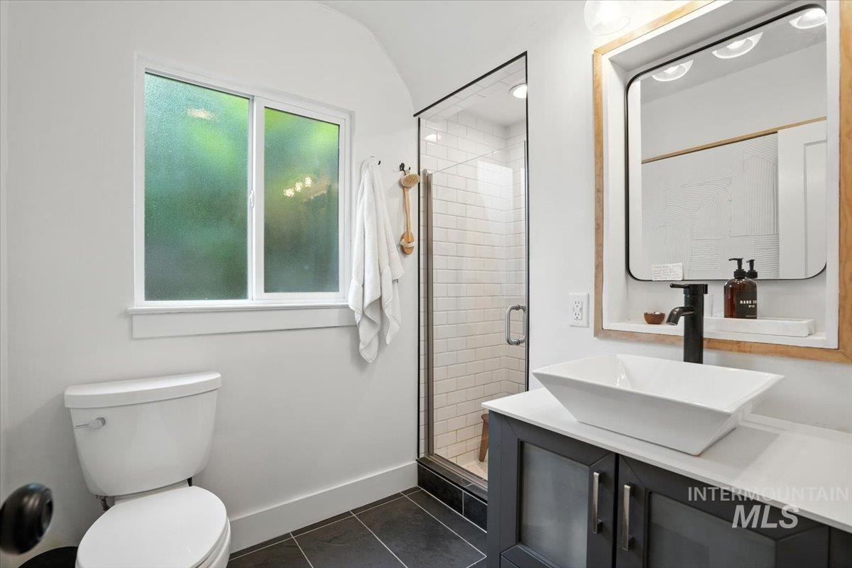 Bathroom featuring a shower stall, vanity, dark tile patterned flooring, and vaulted ceiling
