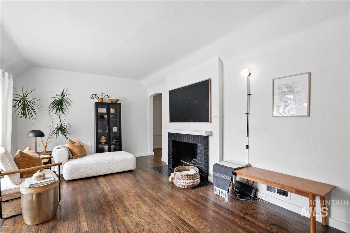 Living area featuring dark wood-style flooring, a brick fireplace, and lofted ceiling