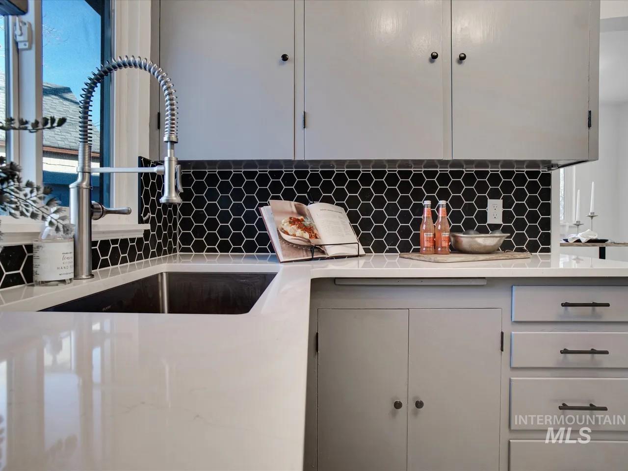 Kitchen with light stone countertops, backsplash, and gray cabinets