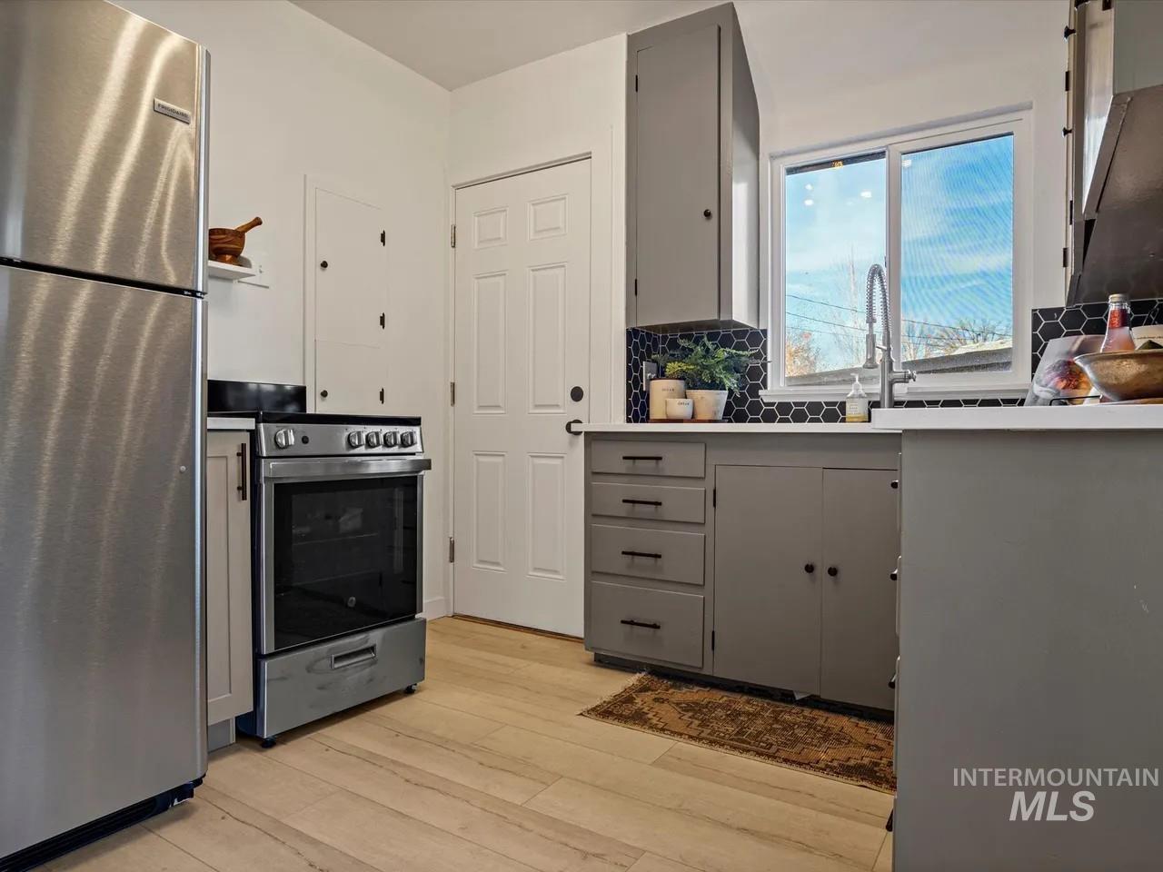 Kitchen featuring gray cabinets, stainless steel appliances, decorative backsplash, and light wood-type flooring