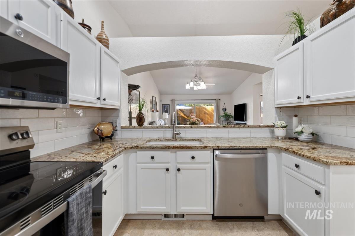 Kitchen with tasteful backsplash, appliances with stainless steel finishes, a chandelier, white cabinets, and light stone counters