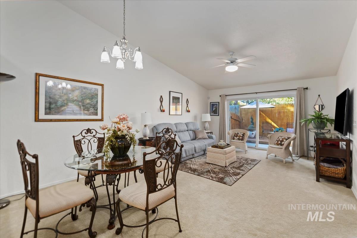 Carpeted dining space with lofted ceiling, a chandelier, and a ceiling fan