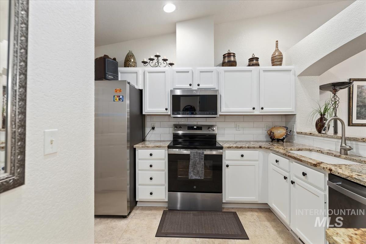 Kitchen with tasteful backsplash, appliances with stainless steel finishes, a textured wall, white cabinets, and light stone countertops