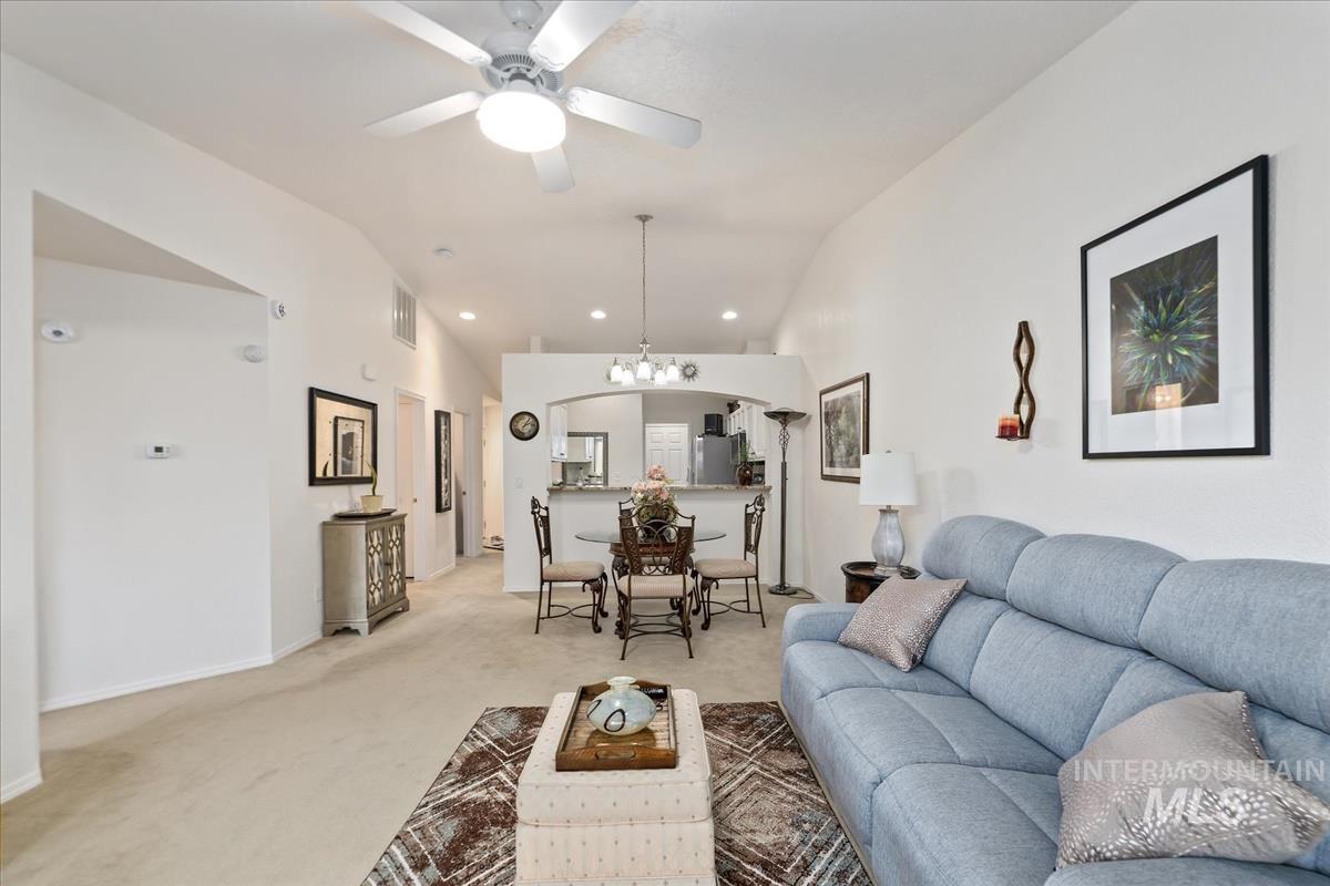 Carpeted living area with vaulted ceiling, a chandelier, ceiling fan, recessed lighting, and arched walkways