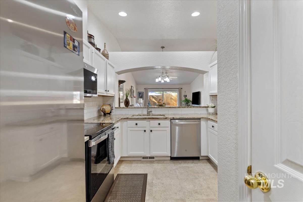 Kitchen featuring appliances with stainless steel finishes, white cabinets, light stone counters, light tile patterned flooring, and tasteful backsplash