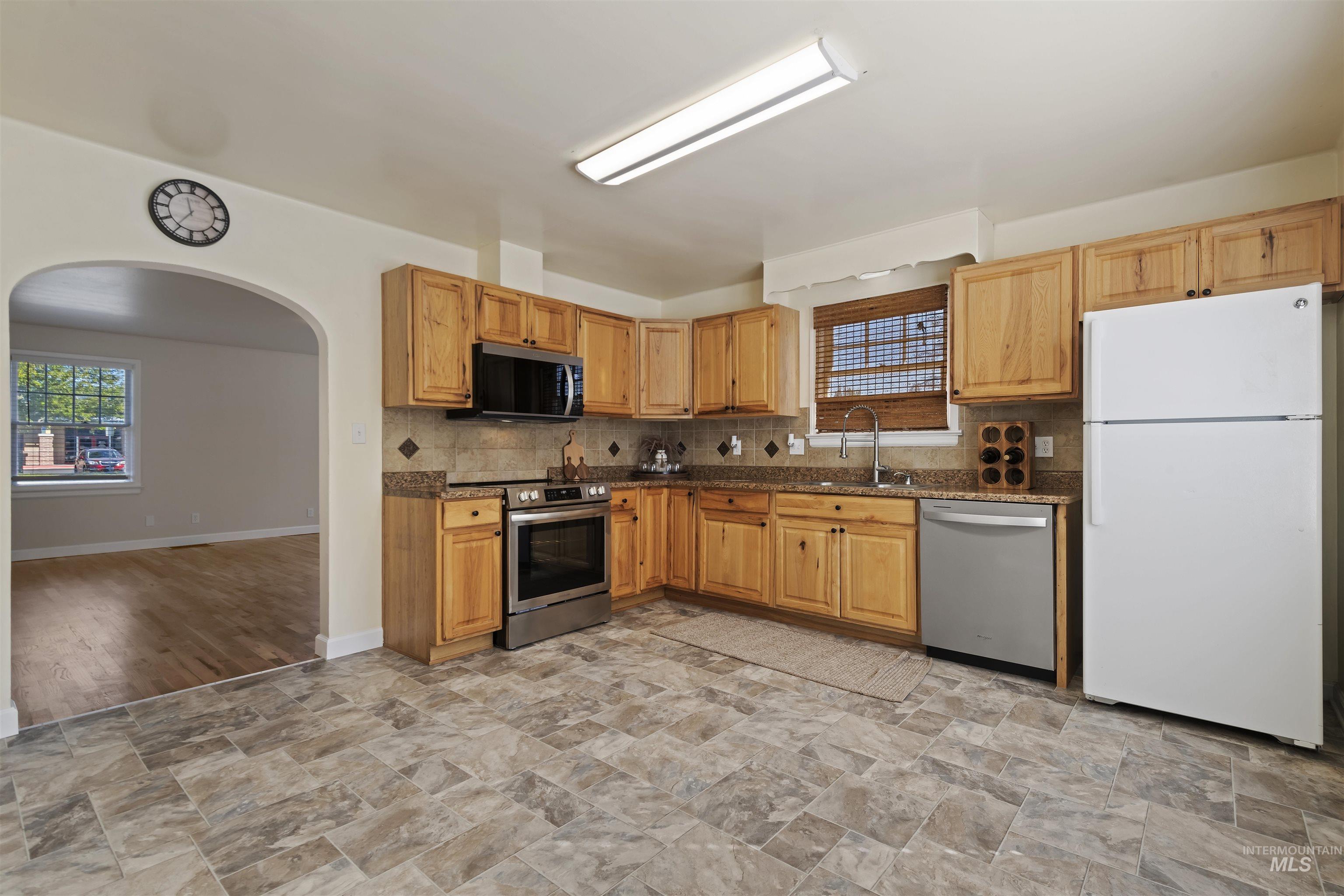Kitchen featuring appliances with stainless steel finishes, tasteful backsplash, arched walkways, and stone finish floors