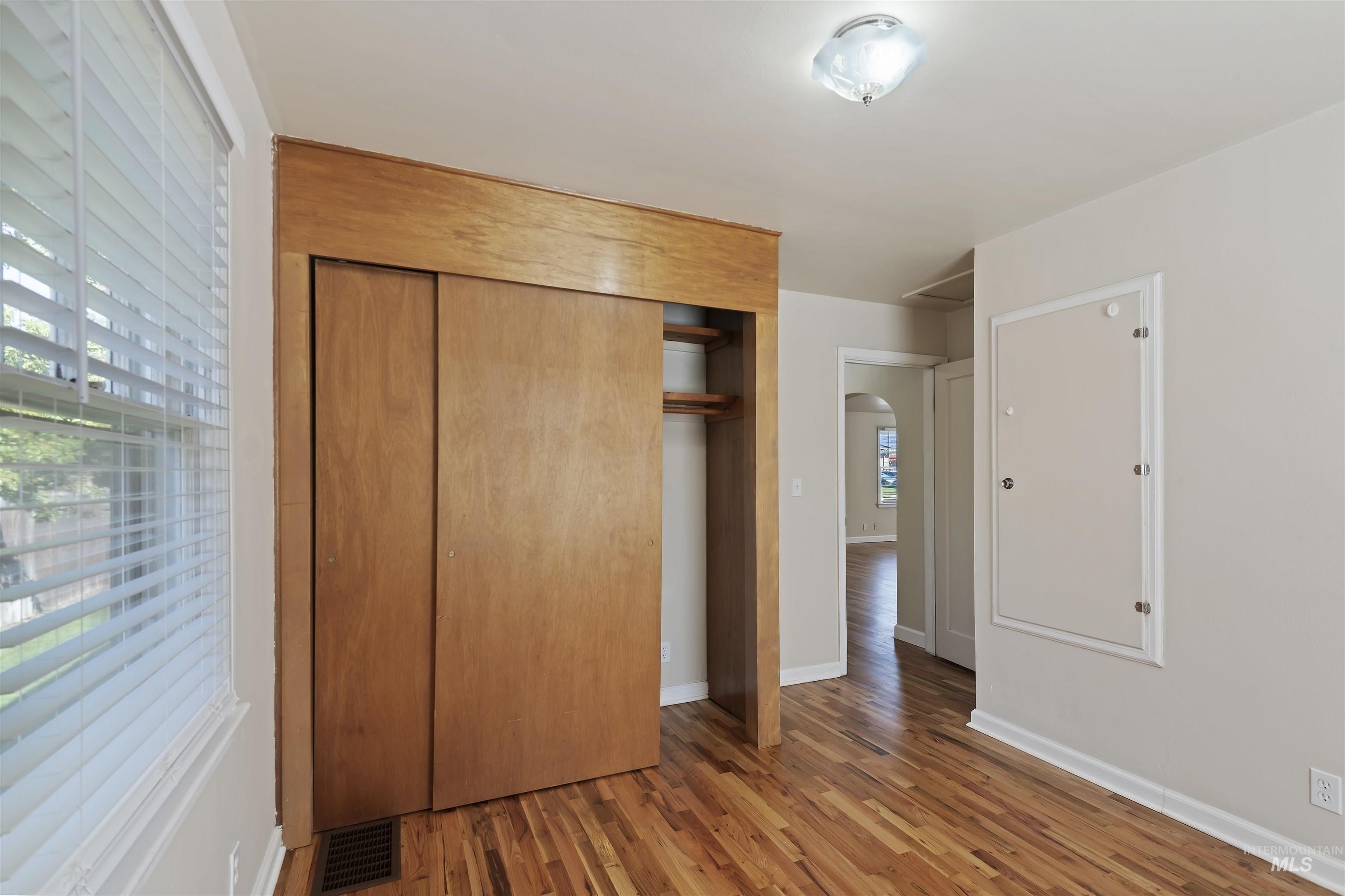 Unfurnished bedroom with arched walkways, wood finished floors, and a closet