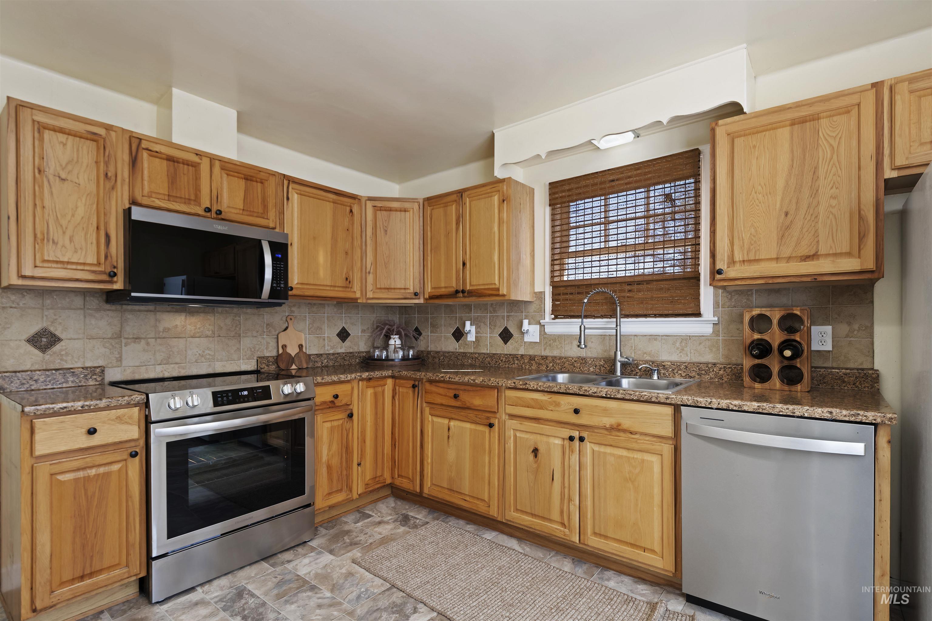 Kitchen featuring stainless steel appliances, backsplash, dark stone counters, and stone finish floors