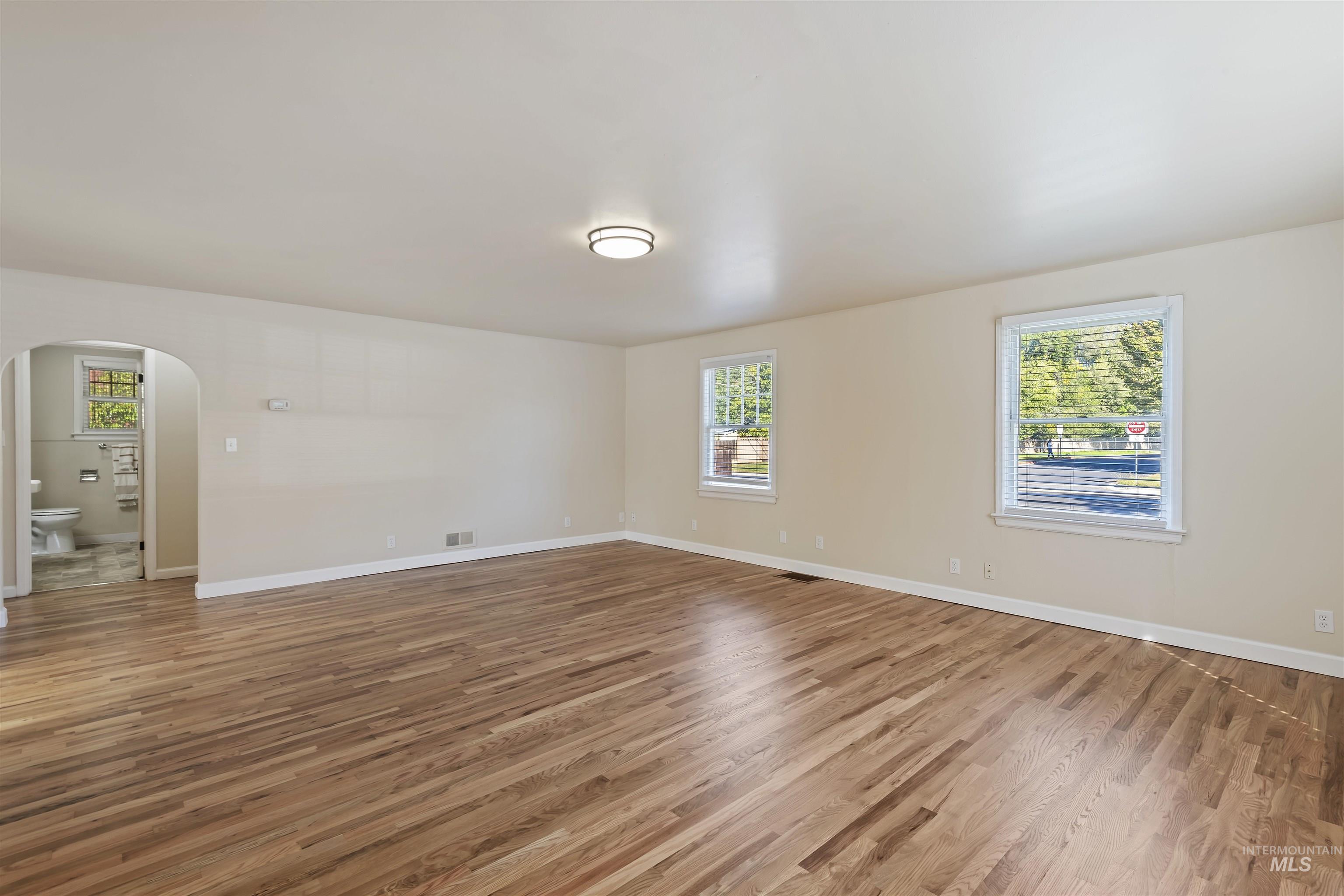 Spare room with arched walkways, healthy amount of natural light, and light wood-style floors