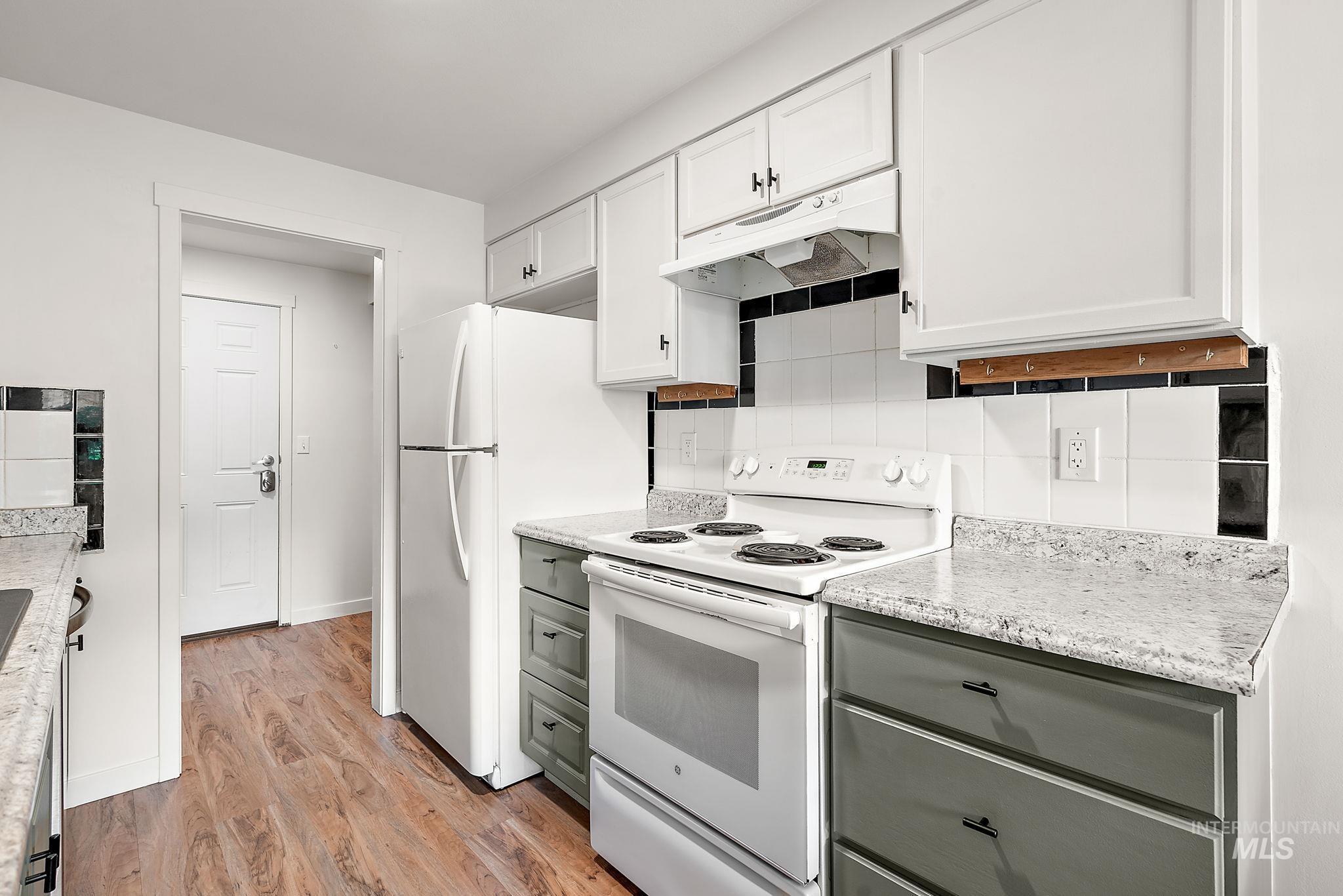 Kitchen featuring white appliances, decorative backsplash, under cabinet range hood, light wood finished floors, and white cabinets