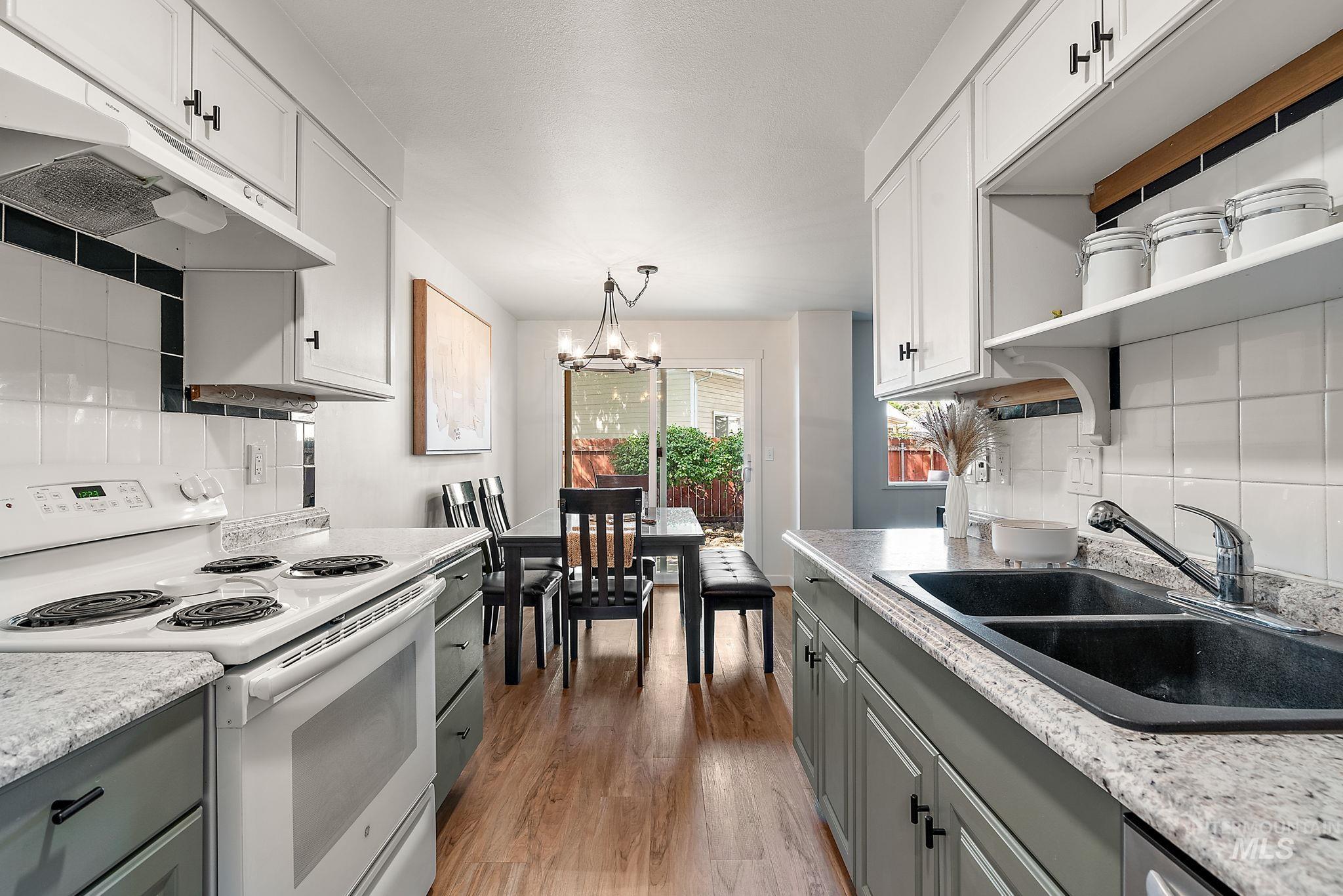 Kitchen with backsplash, white range with electric cooktop, a chandelier, and under cabinet range hood