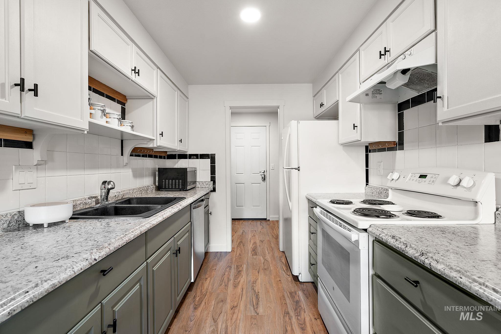 Kitchen with appliances with stainless steel finishes, decorative backsplash, under cabinet range hood, light wood-type flooring, and gray cabinetry