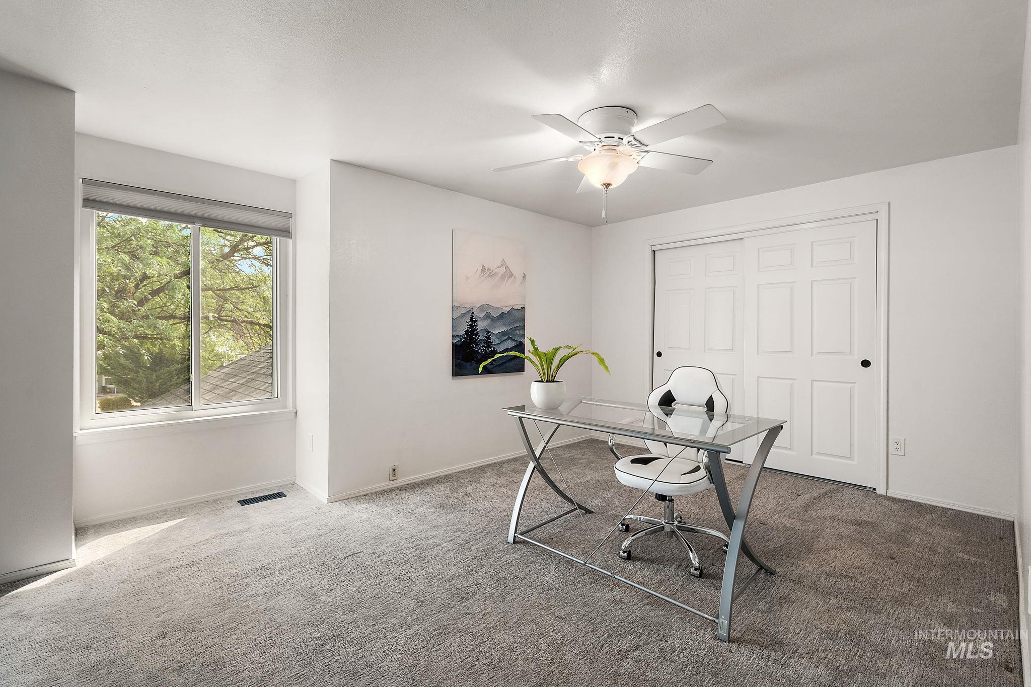Carpeted office space featuring ceiling fan and baseboards