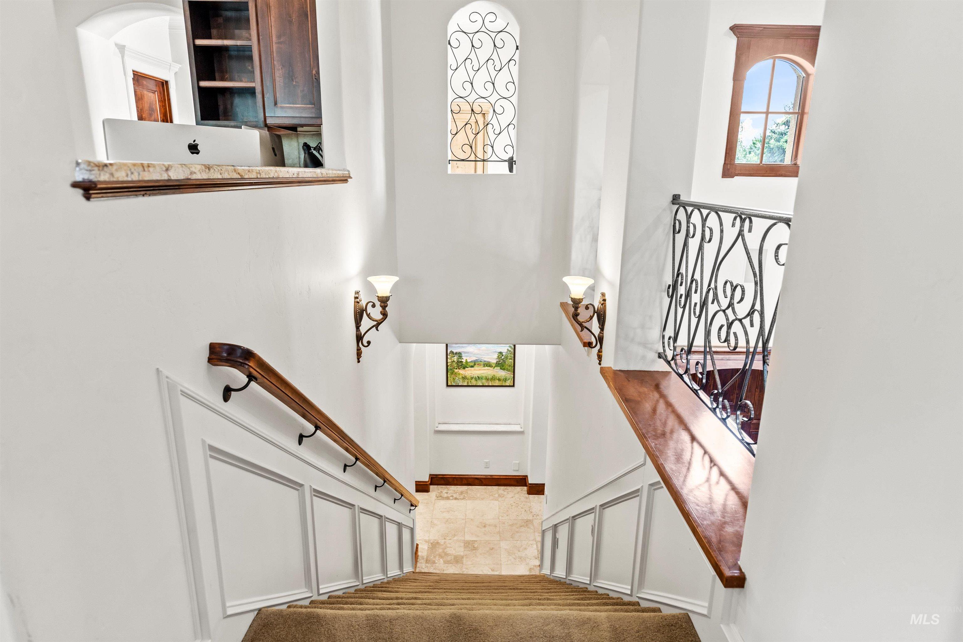 Multi-level interior featuring a carpeted staircase with a wood handrail, white wainscoting, and decorative wrought iron railing