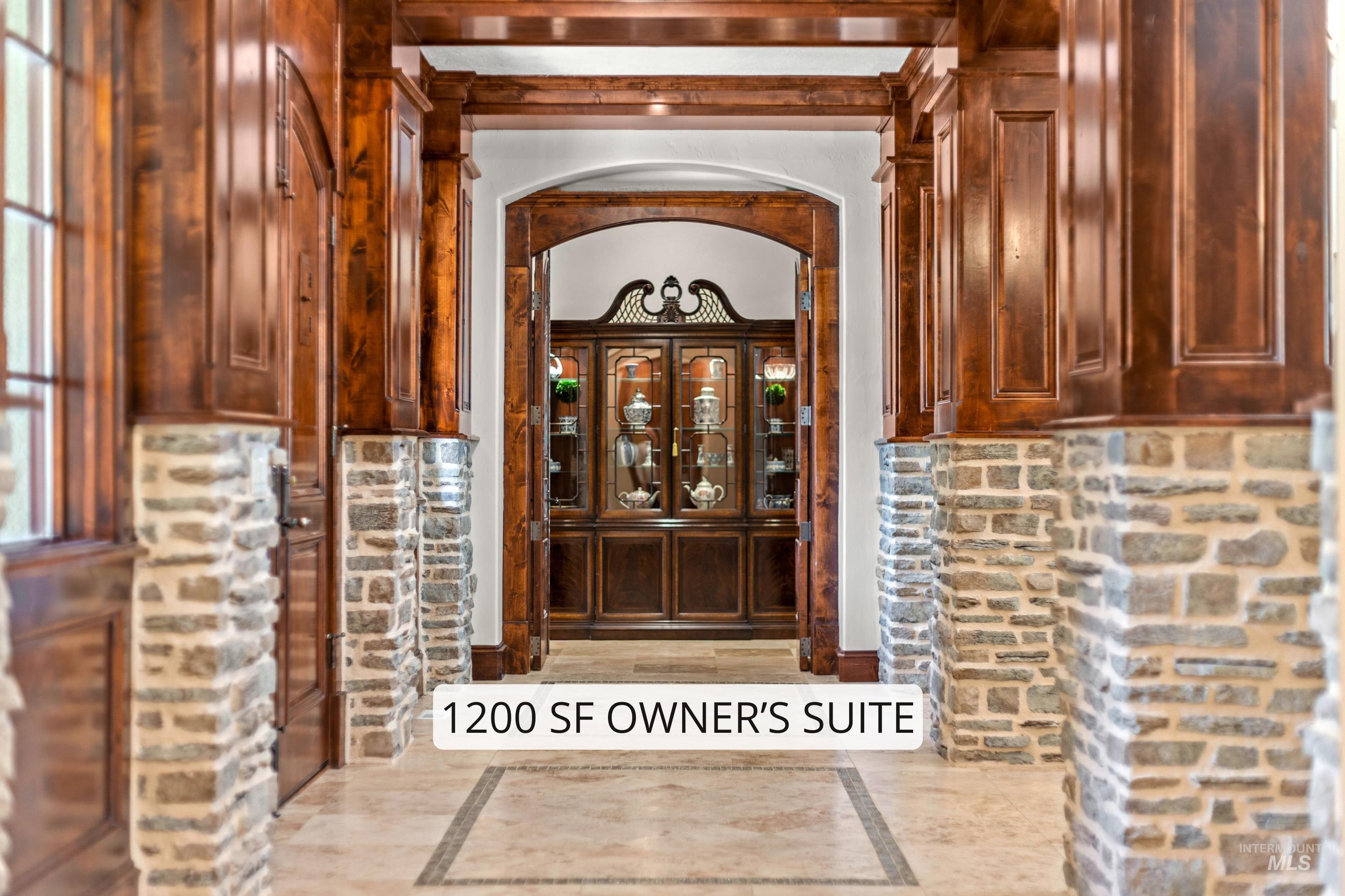 Grand hallway featuring stone-clad pillars, rich wood paneling, arched doorways, a coffered ceiling, and tile flooring with an intricate inlay design