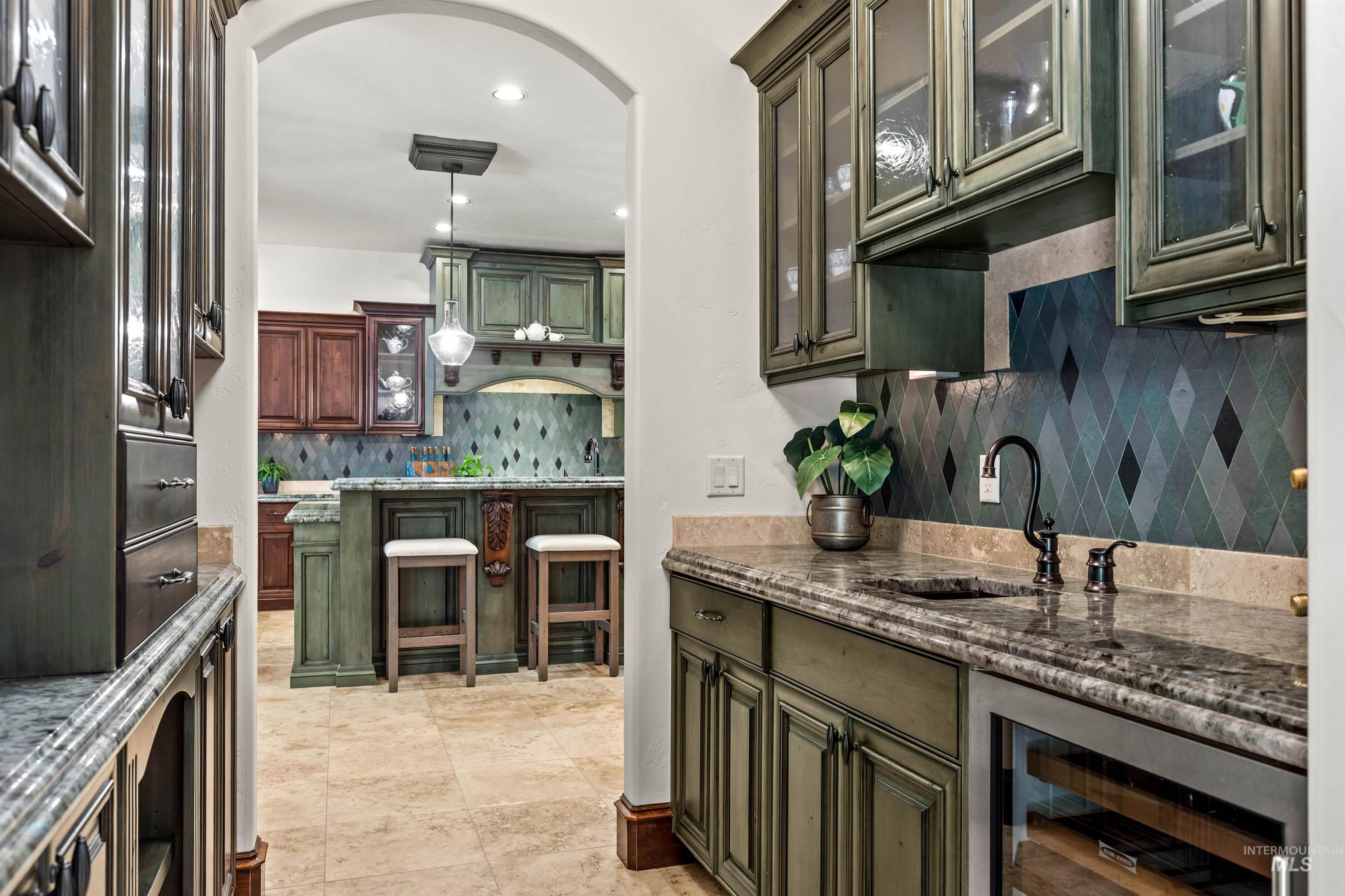 Pass-through wet bar featuring distressed green cabinetry, an under-counter beverage cooler, and a stone countertop