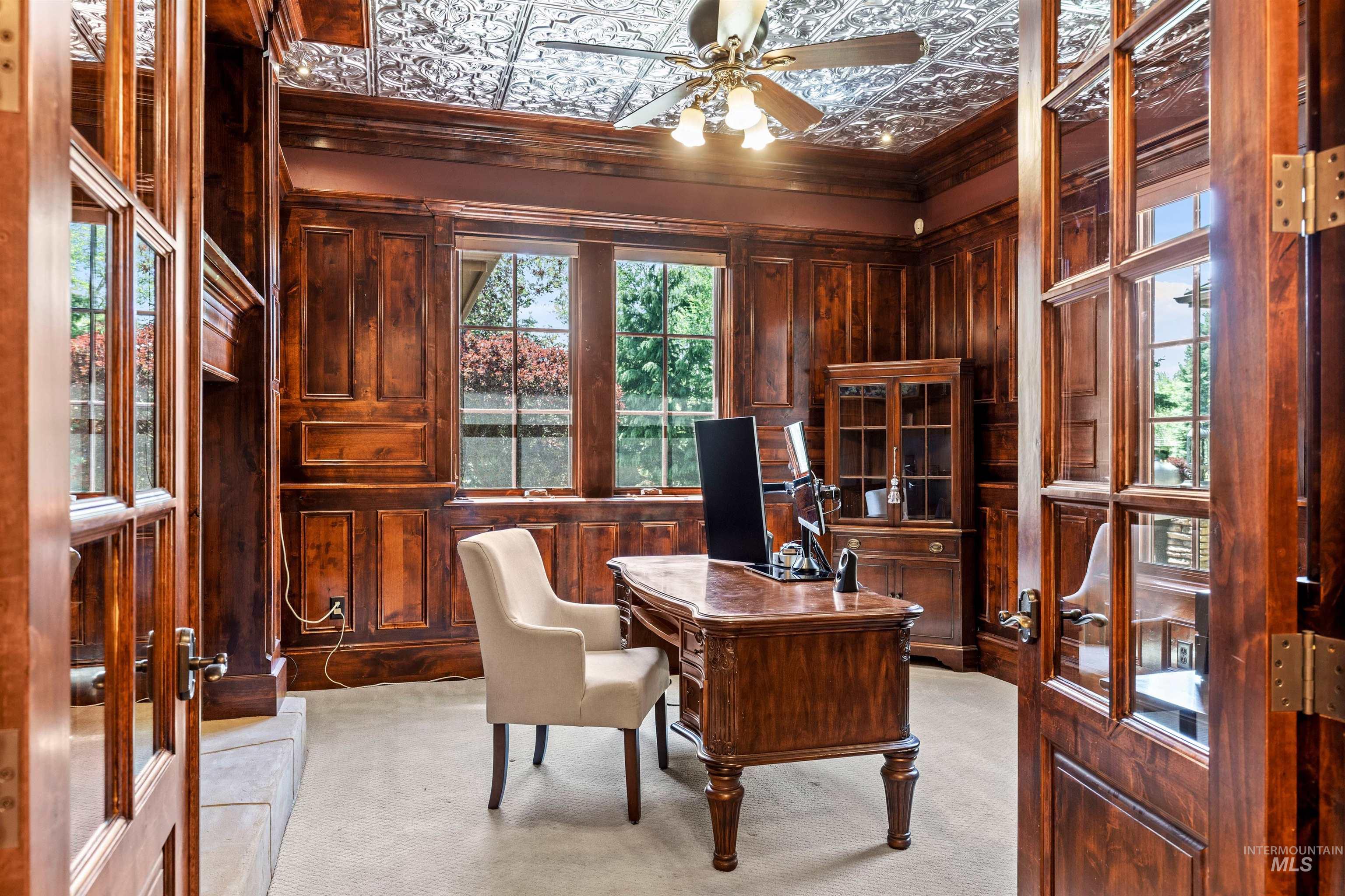 Wood-paneled room featuring a decorative tin ceiling, a multi-pane window with exterior greenery, and a built-in display cabinet