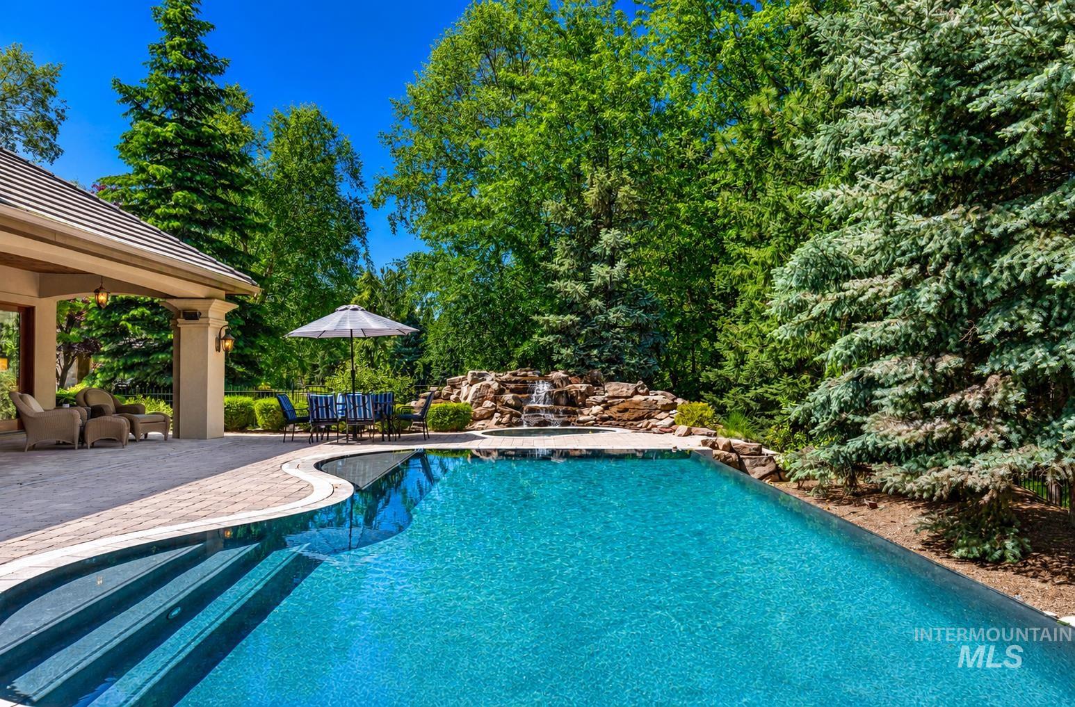 Inviting outdoor space featuring a curvilinear swimming pool, expansive paved patio, and a stone waterfall
