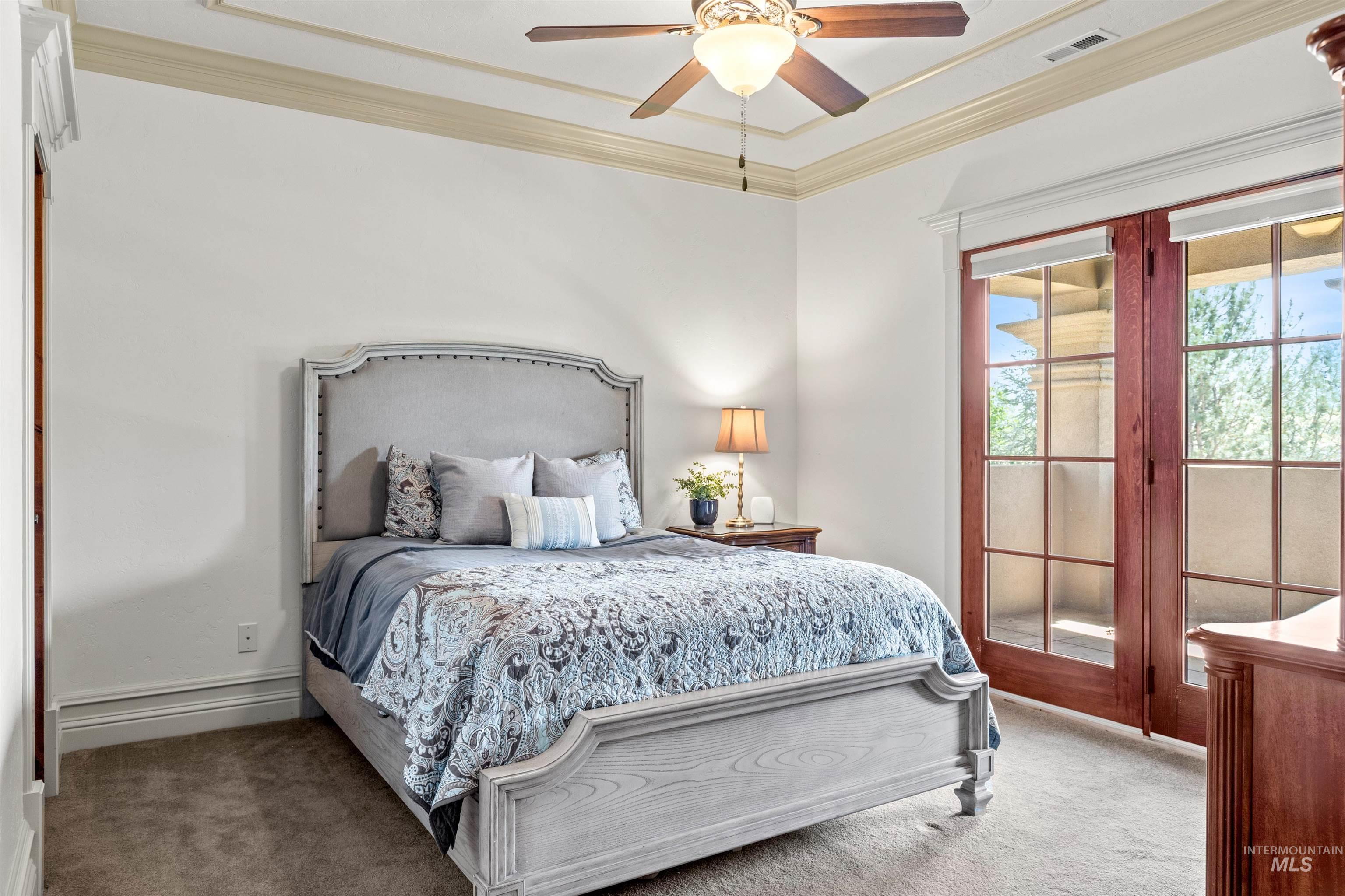 Hardwood French doors opening to a private balcony, complemented by crown molding, tray ceiling, and a ceiling fan with integrated lighting