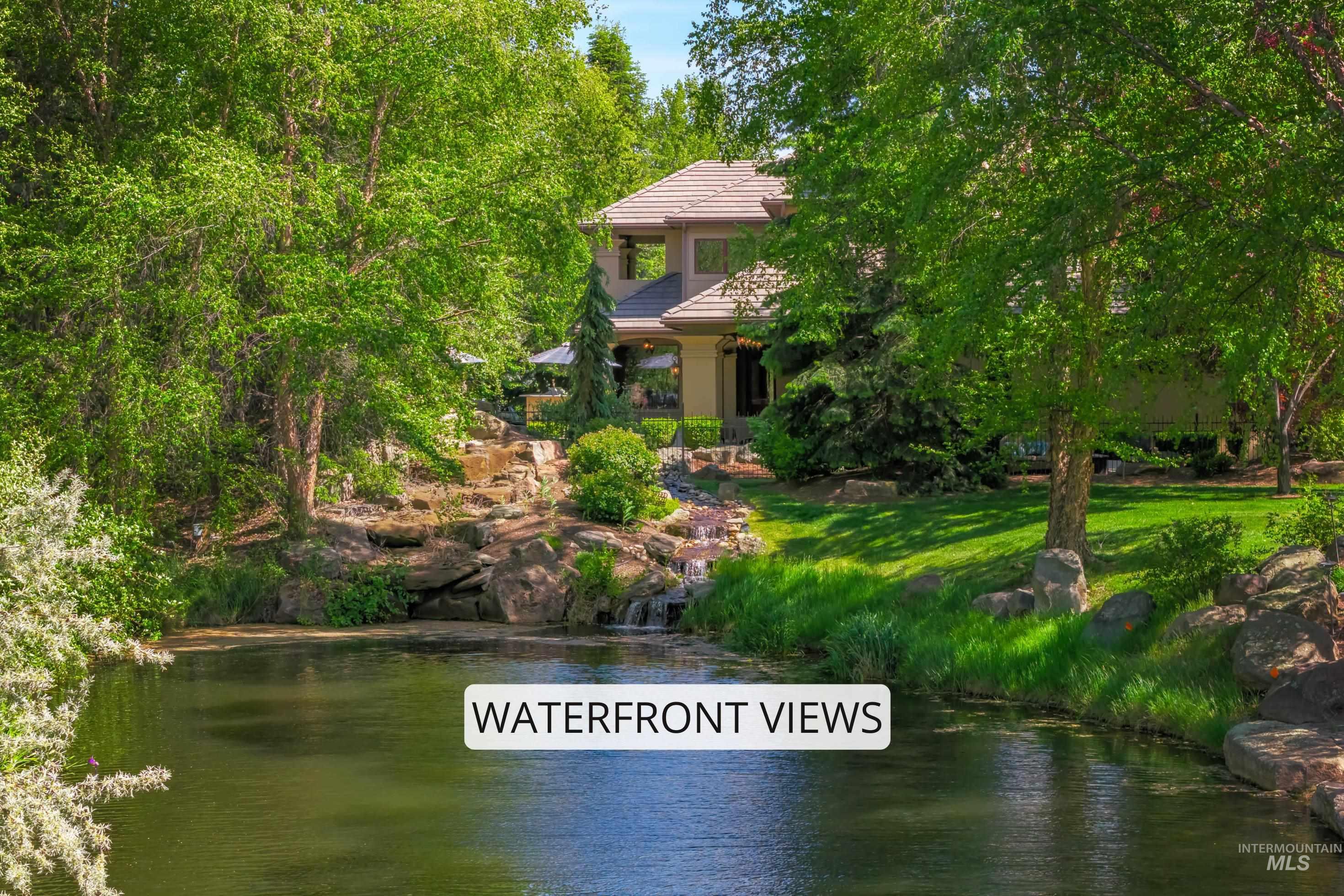 Waterfront property featuring a tiered rock waterfall, mature green trees, and a manicured lawn