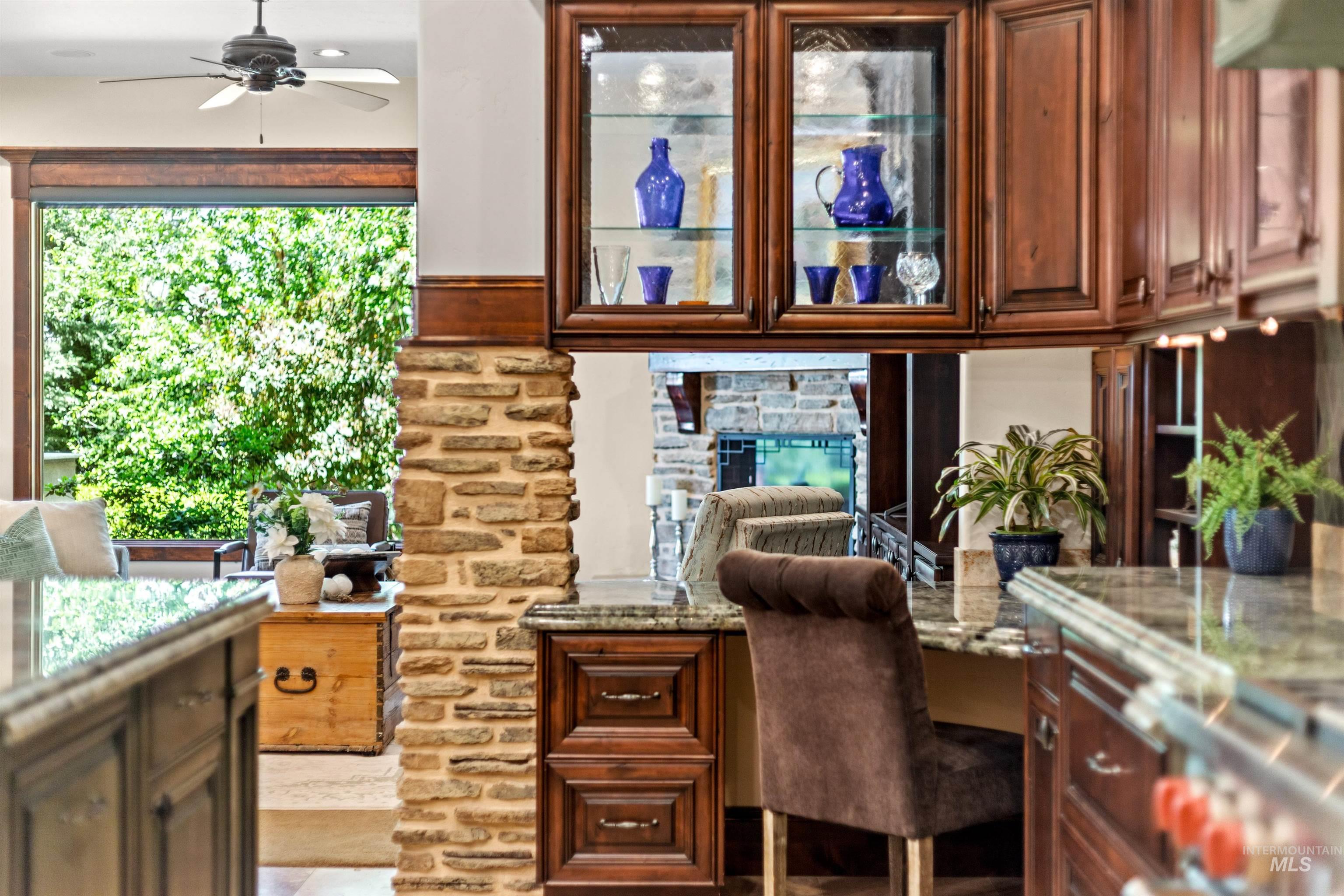 Kitchen featuring rich wood cabinetry, stone column accents, display cabinets with glass fronts, and granite countertops