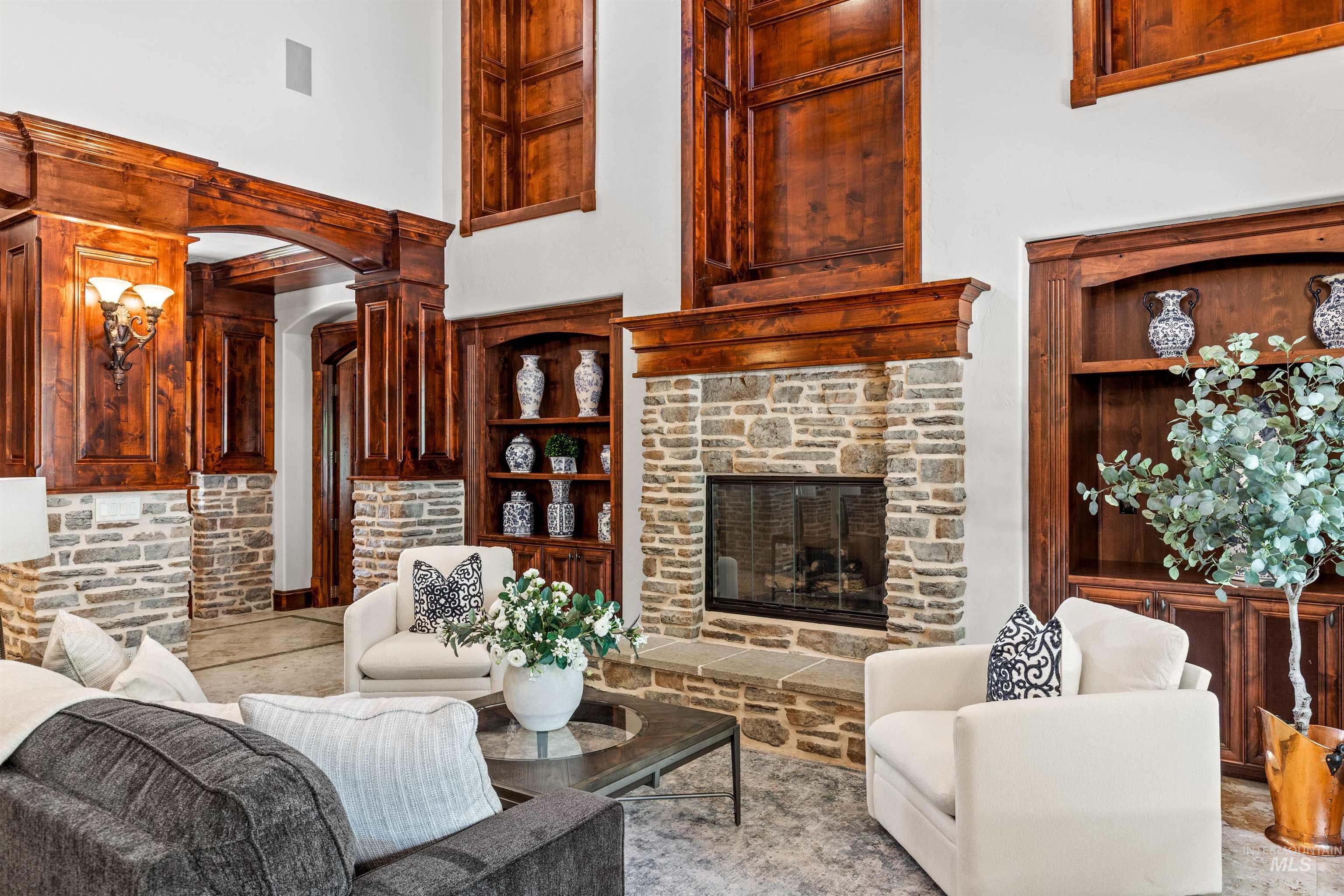 Living area featuring a stone fireplace with a wood mantle, built-in wooden shelving, and high ceilings with decorative wood paneling