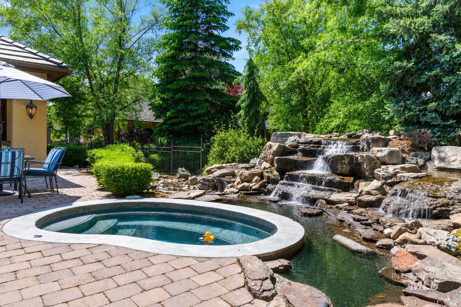 Outdoor spa with a natural rock waterfall feature and surrounding mature landscaping