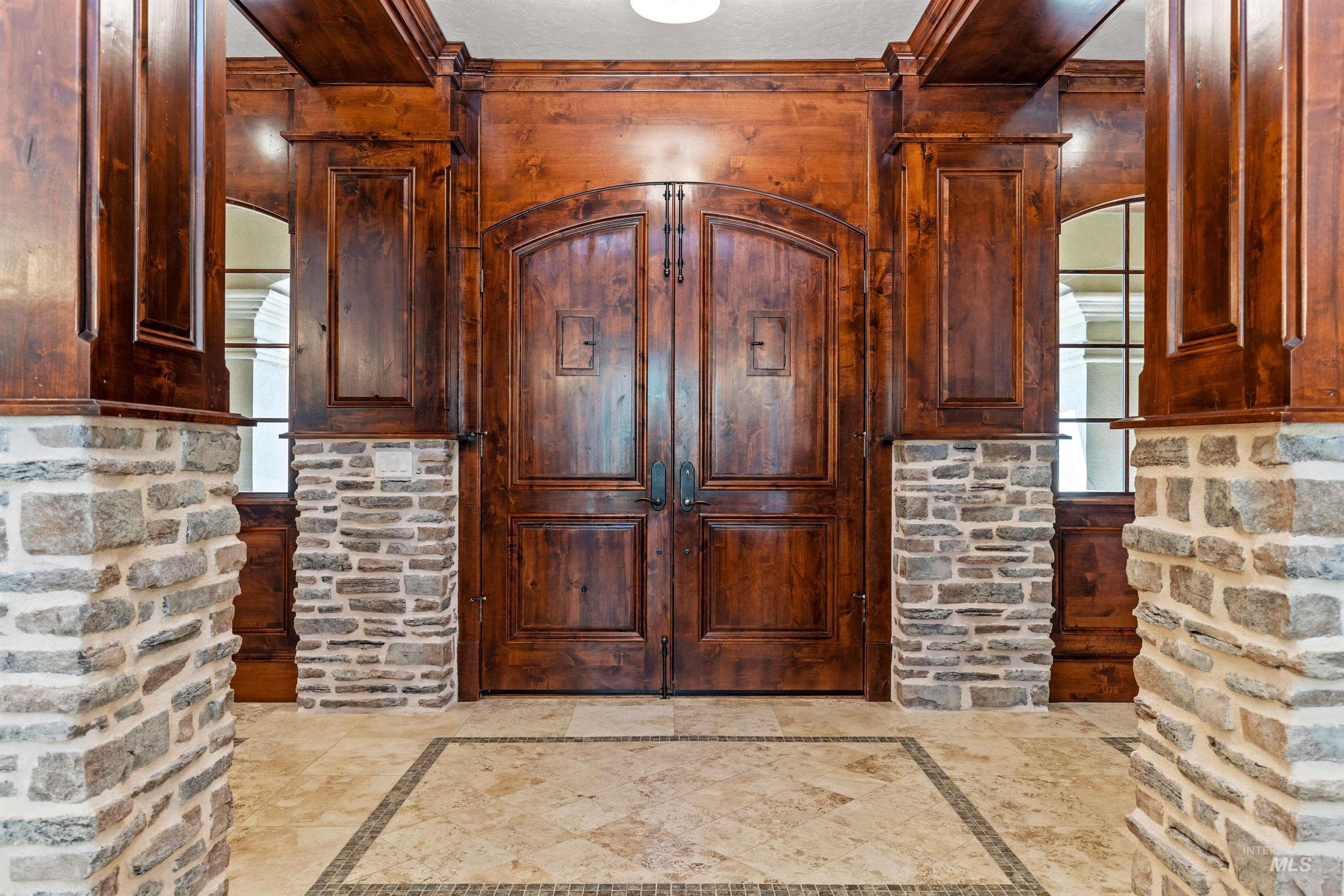Arch-top double entry doors in a rich wood-tone finish, framed by stone veneer columns and extensive wood paneling