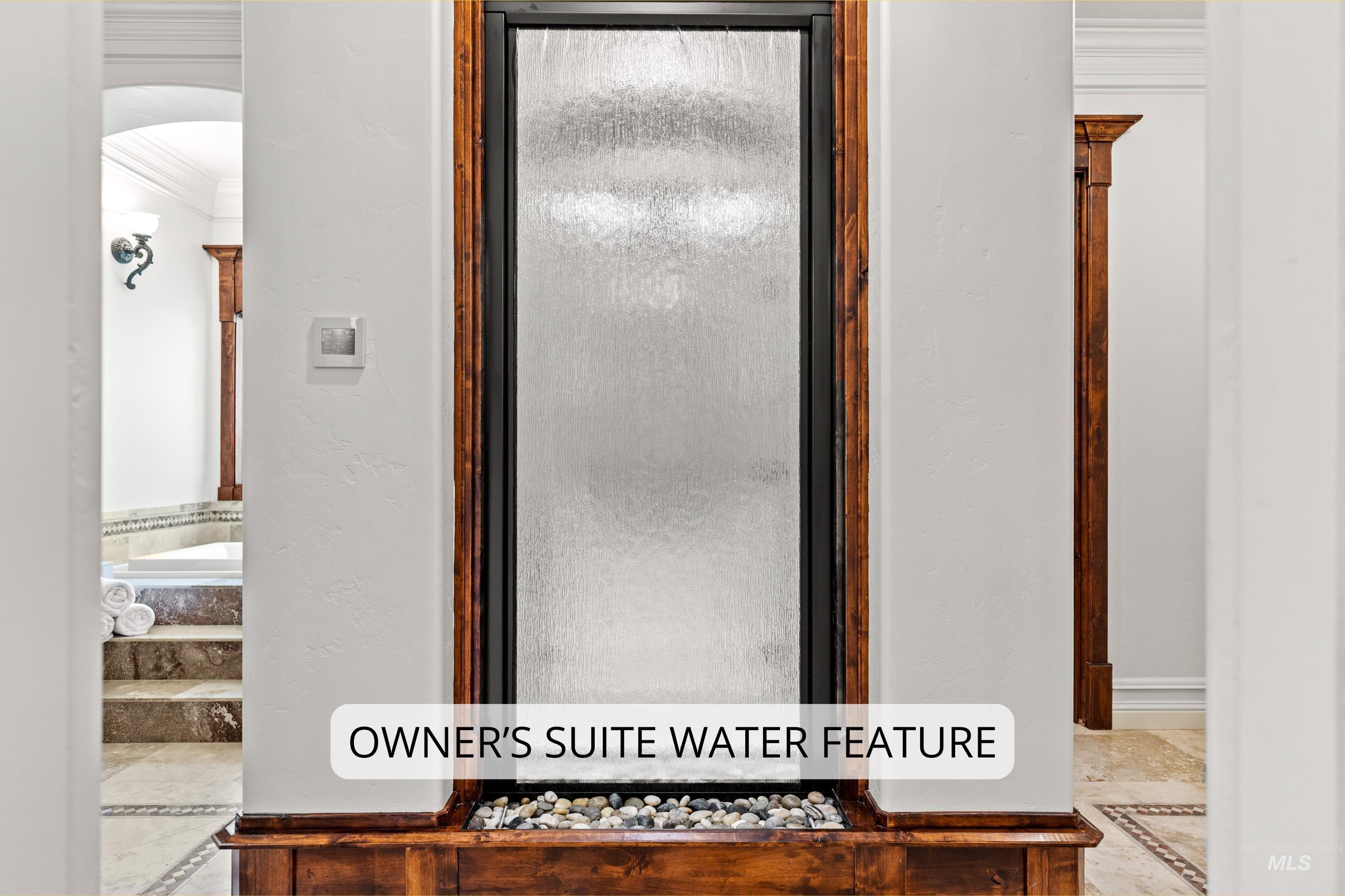 Built-in water feature with wood-finish frame, pebble base, and textured glass panel