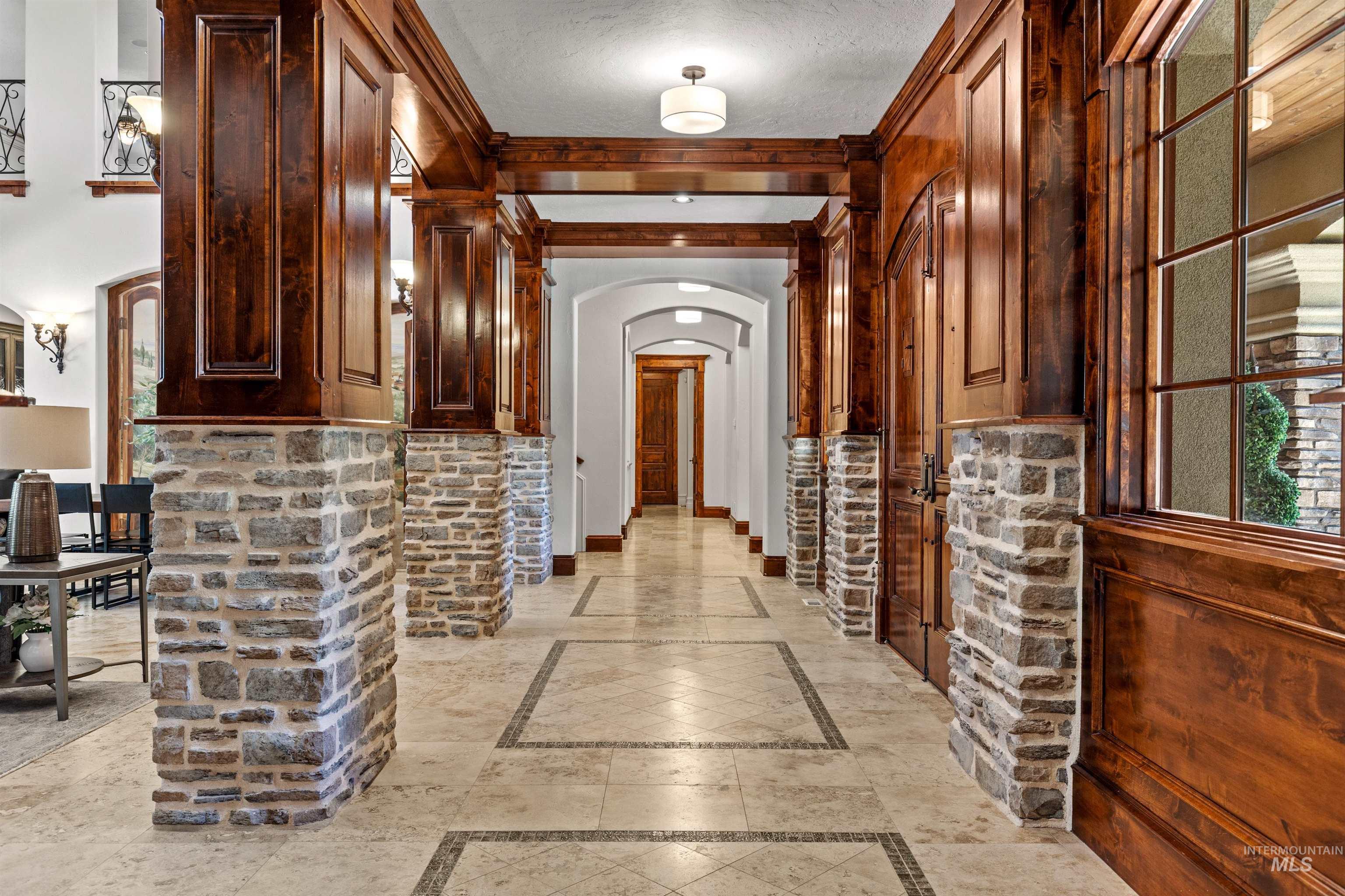 Grand hallway featuring stone column bases, rich wood paneling, recessed archways, an arched doorway, and patterned tile flooring