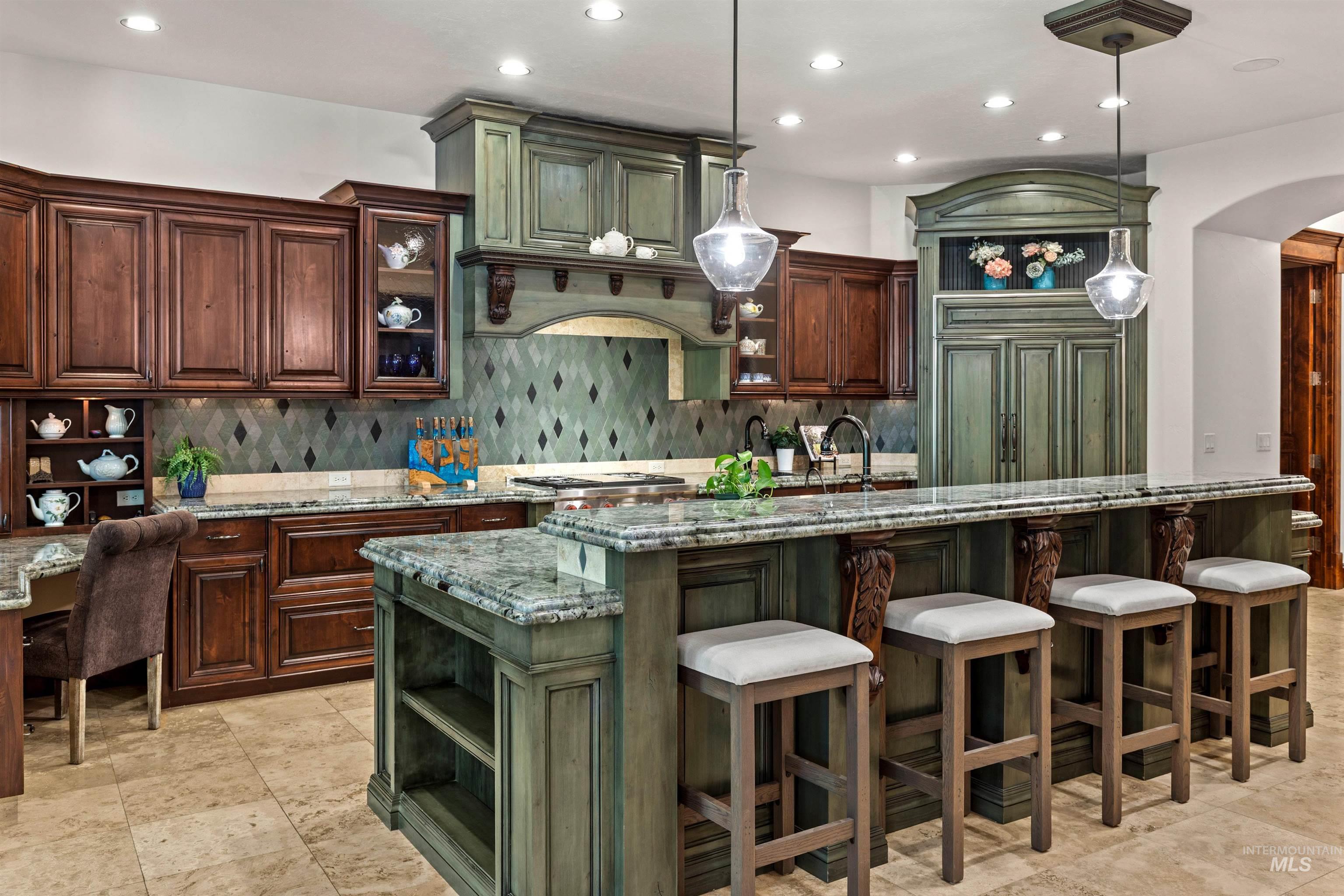 Spacious kitchen featuring a large central island with seating, pendant lighting, two-tone cabinetry, light-colored countertops, and a patterned backsplash