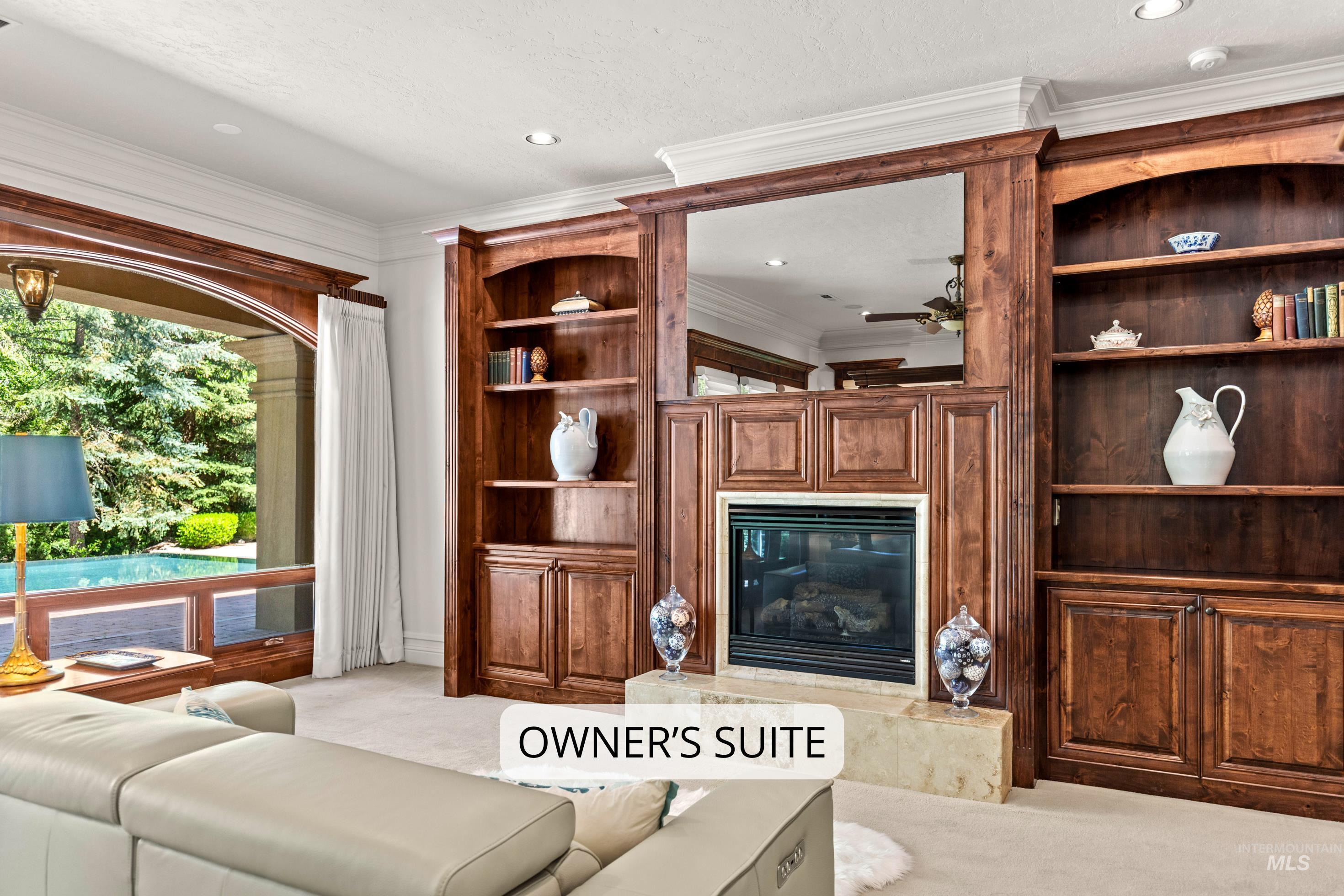 Living area featuring a stone-faced fireplace with a wood-paneled surround, integrated shelving, built-in cabinetry, and crown molding