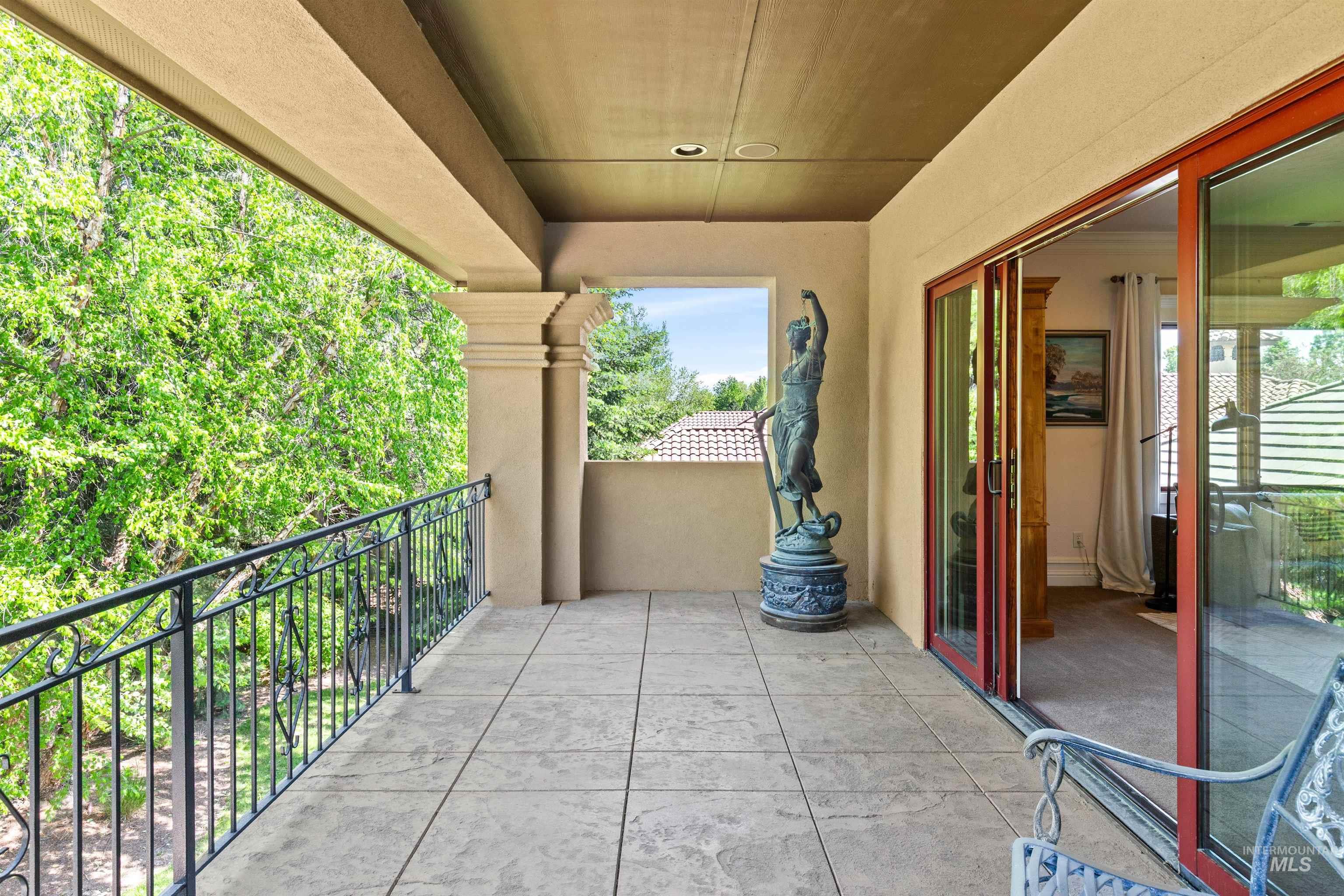 Spacious covered patio with textured tile flooring, wrought iron railing, and stucco columns