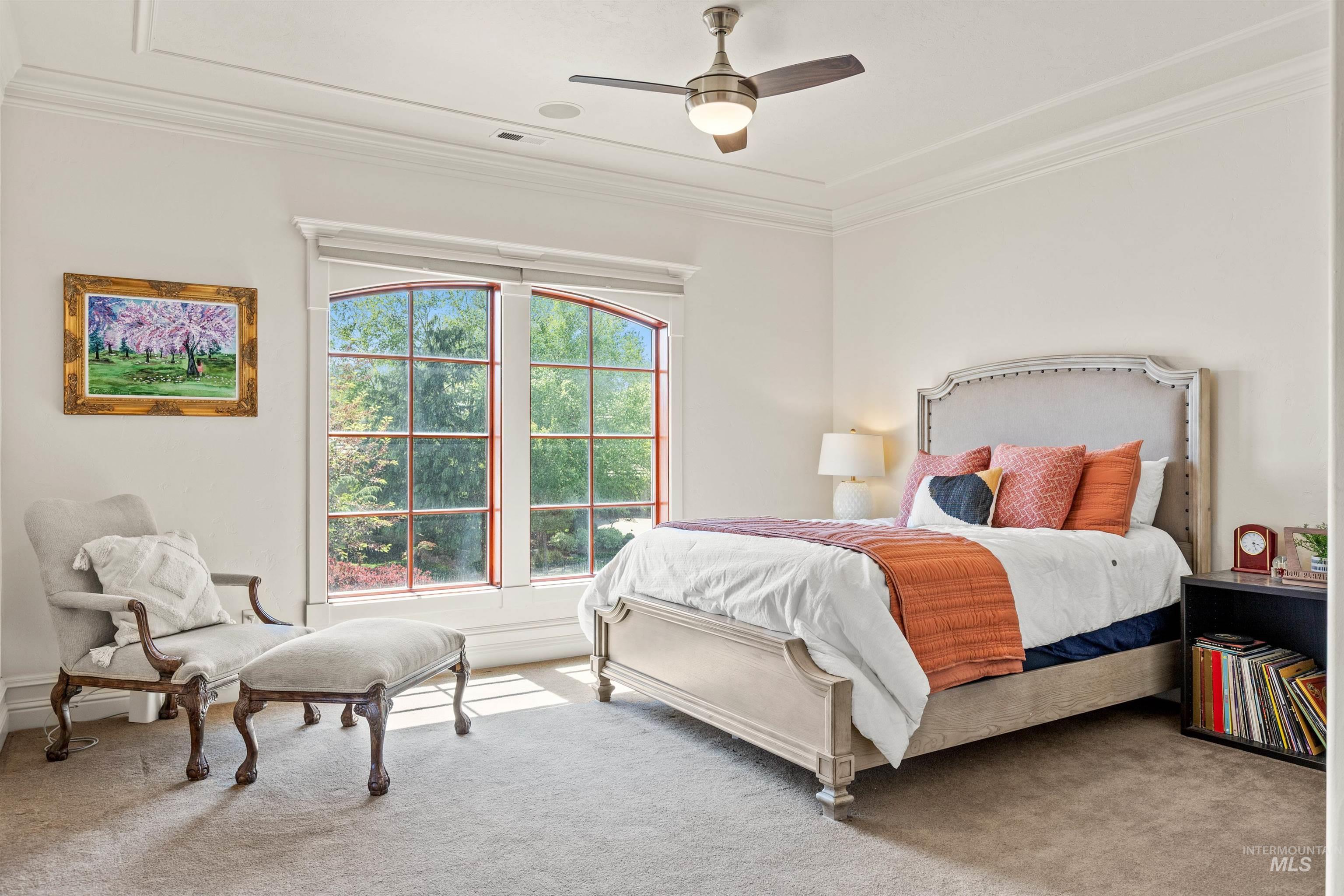 Bedroom featuring large arched windows, crown molding, a ceiling fan with integrated lighting, and plush carpeting