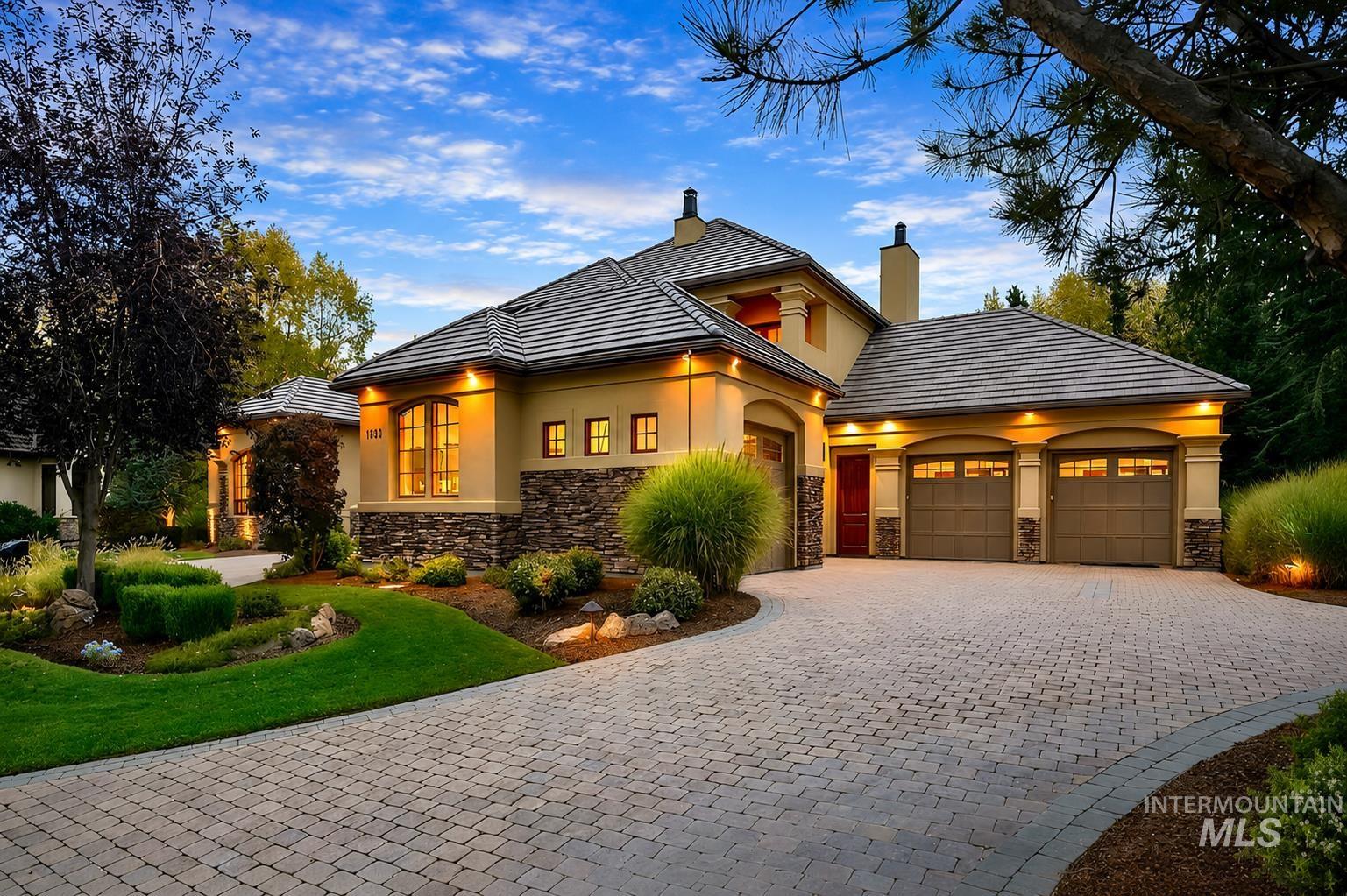 Stucco exterior with stone accenting, tile roofing, a paver driveway, and an attached three-car garage