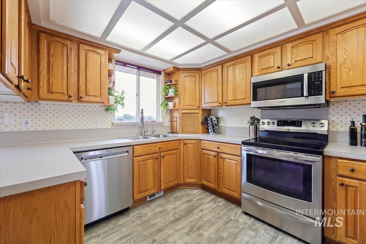Kitchen featuring appliances with stainless steel finishes, tasteful backsplash, brown cabinets, and light countertops