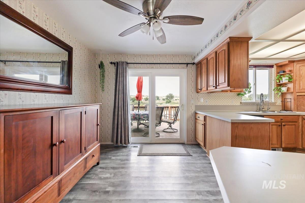Kitchen with light countertops, light wood-type flooring, wallpapered walls, a ceiling fan, and brown cabinets