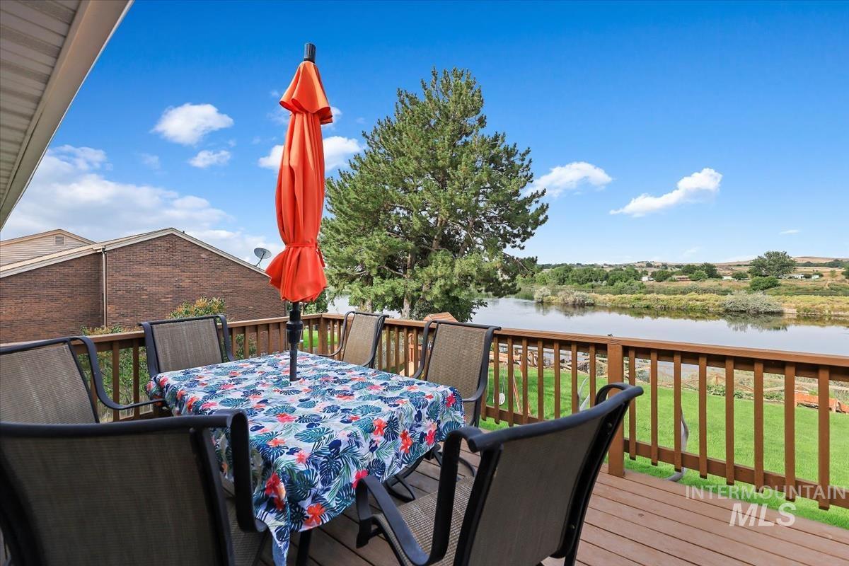 Wooden terrace featuring outdoor dining space, a water view, and a yard