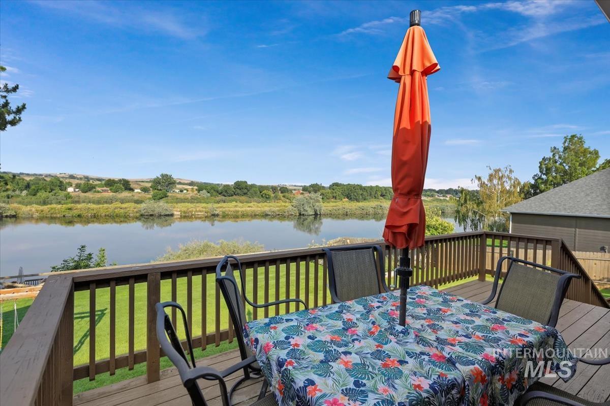 Wooden terrace with outdoor dining area, a water view, and a lawn