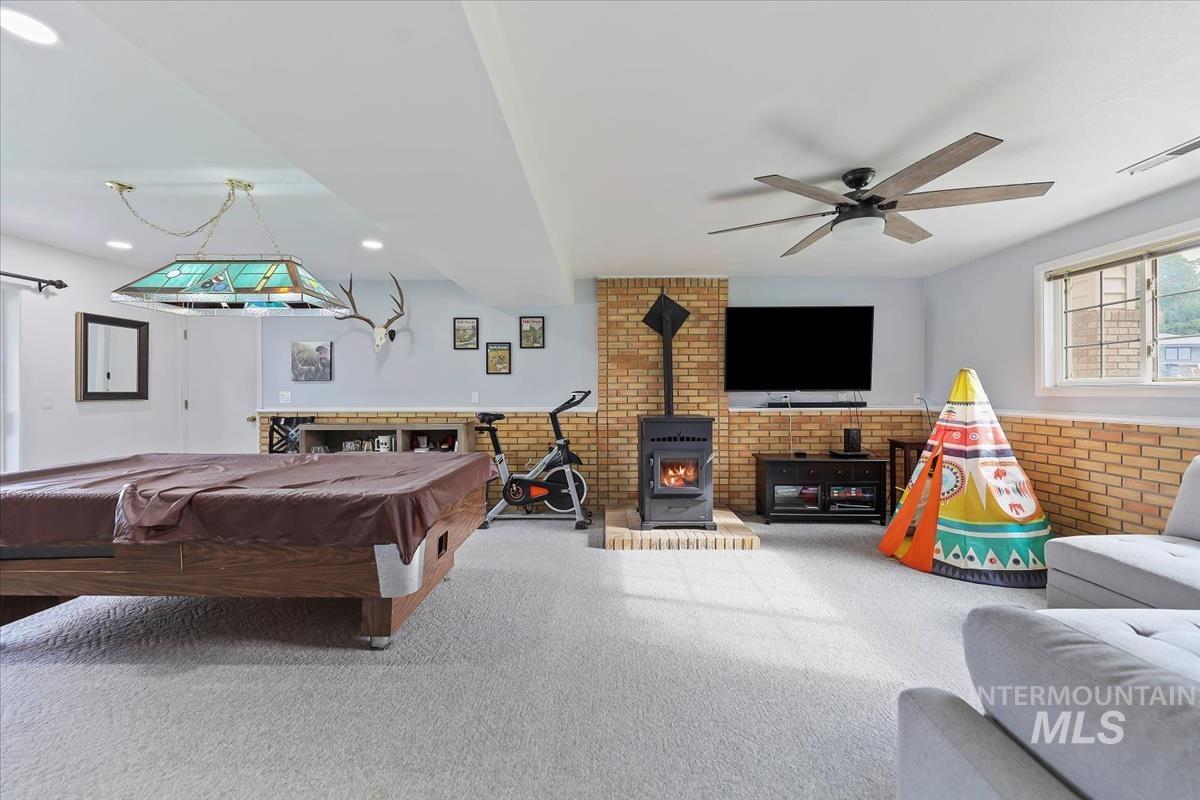 Recreation room with a wood stove, billiards table, brick wall, and carpet floors