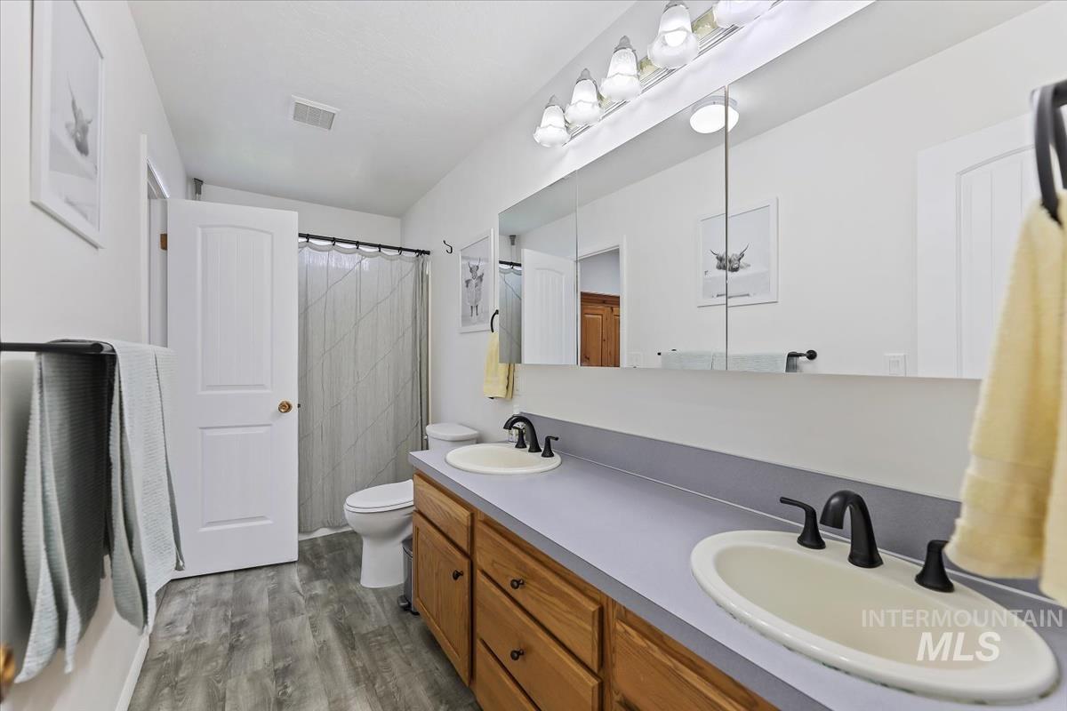 Full bath featuring double vanity, light wood finished floors, and a shower with curtain
