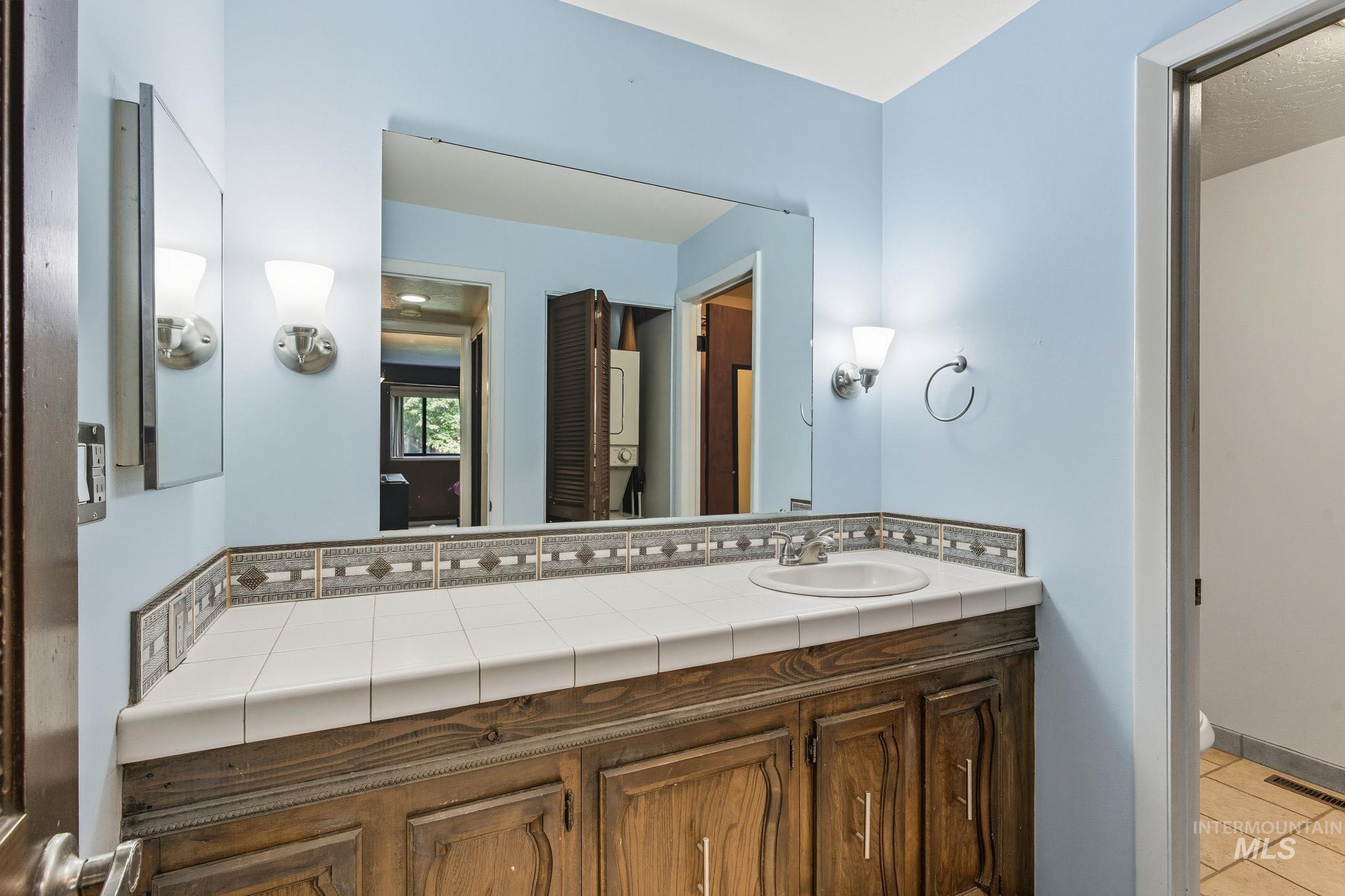 Bathroom with vanity, light tile patterned floors, and stacked washing machine and dryer