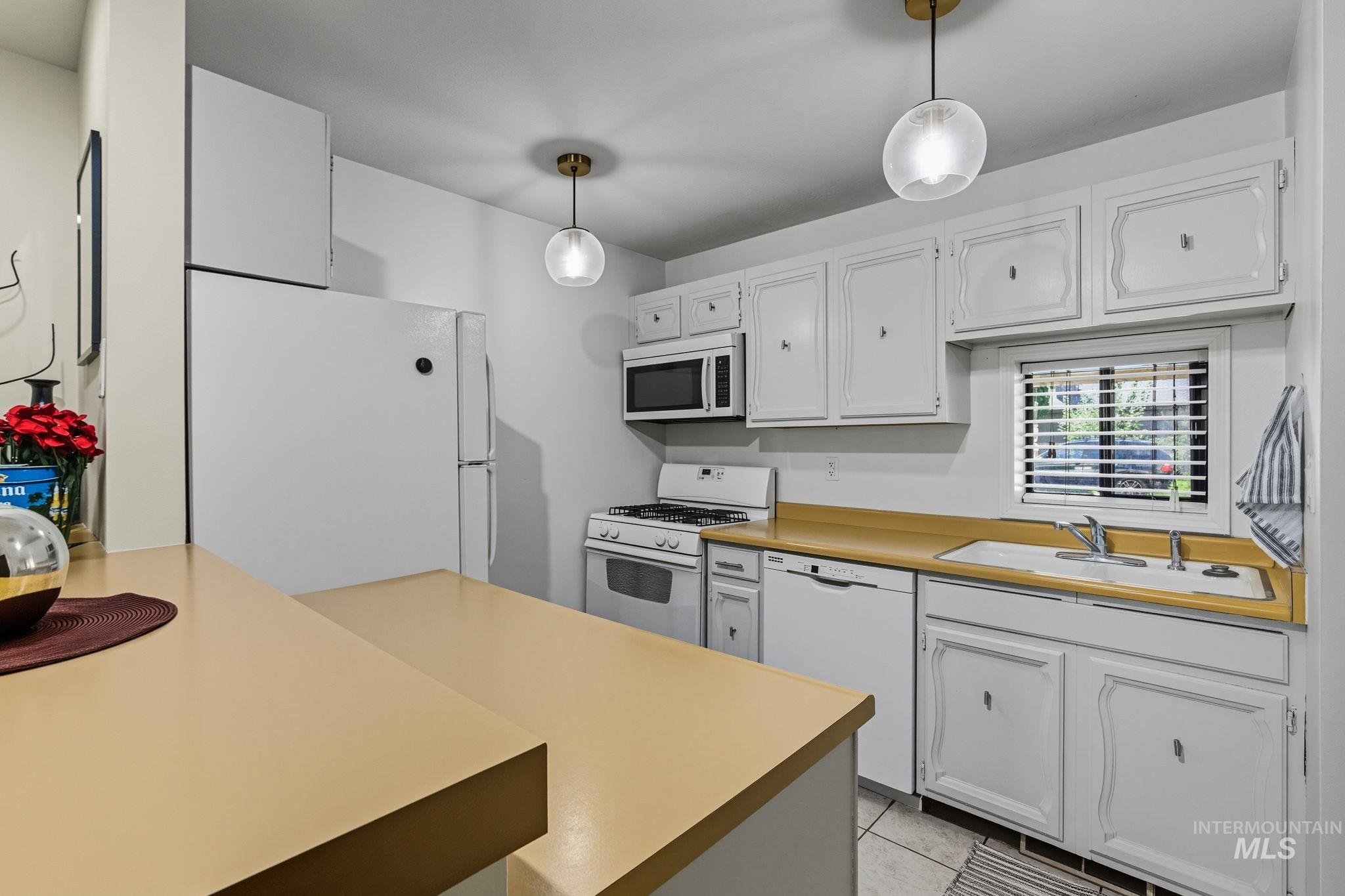 Kitchen featuring white appliances, white cabinetry, hanging light fixtures, and light countertops