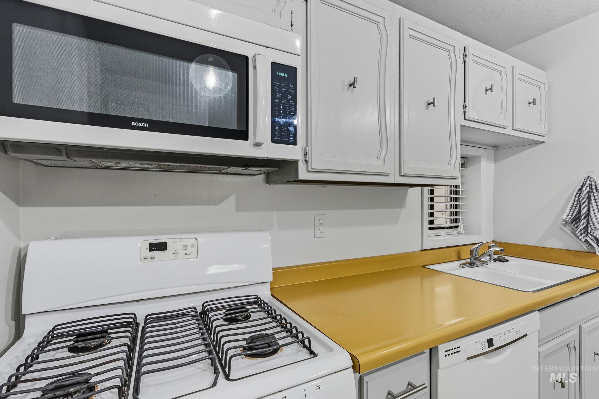 Kitchen featuring white appliances, light countertops, and white cabinets
